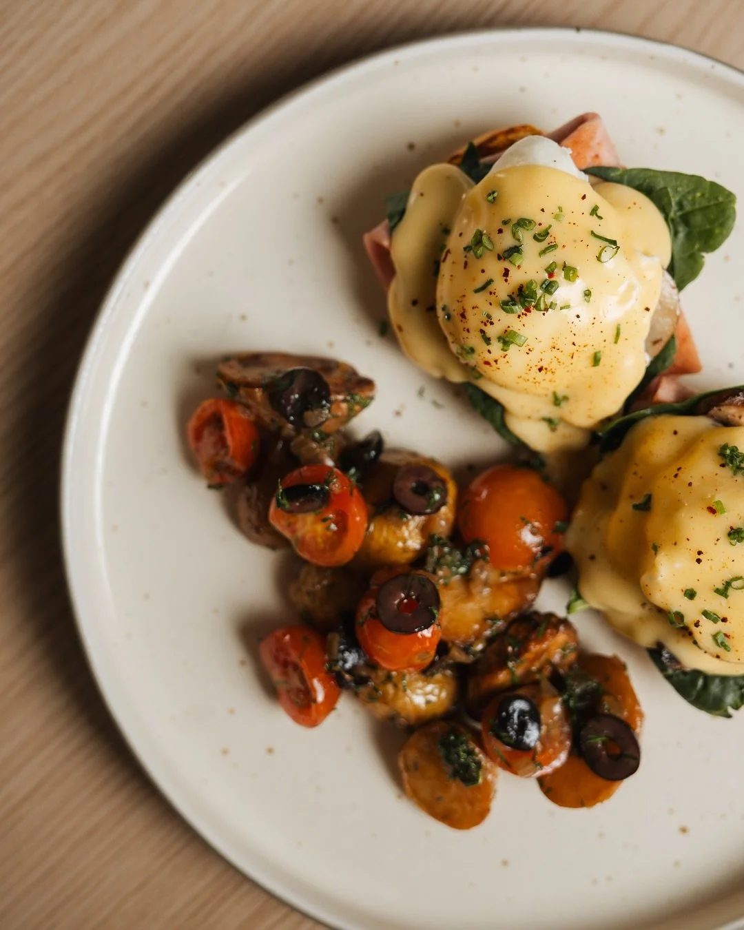 Eggs Benedict with hollandaise sauce, spinach, and ham, served with roasted cherry tomatoes and sautéed mushrooms.