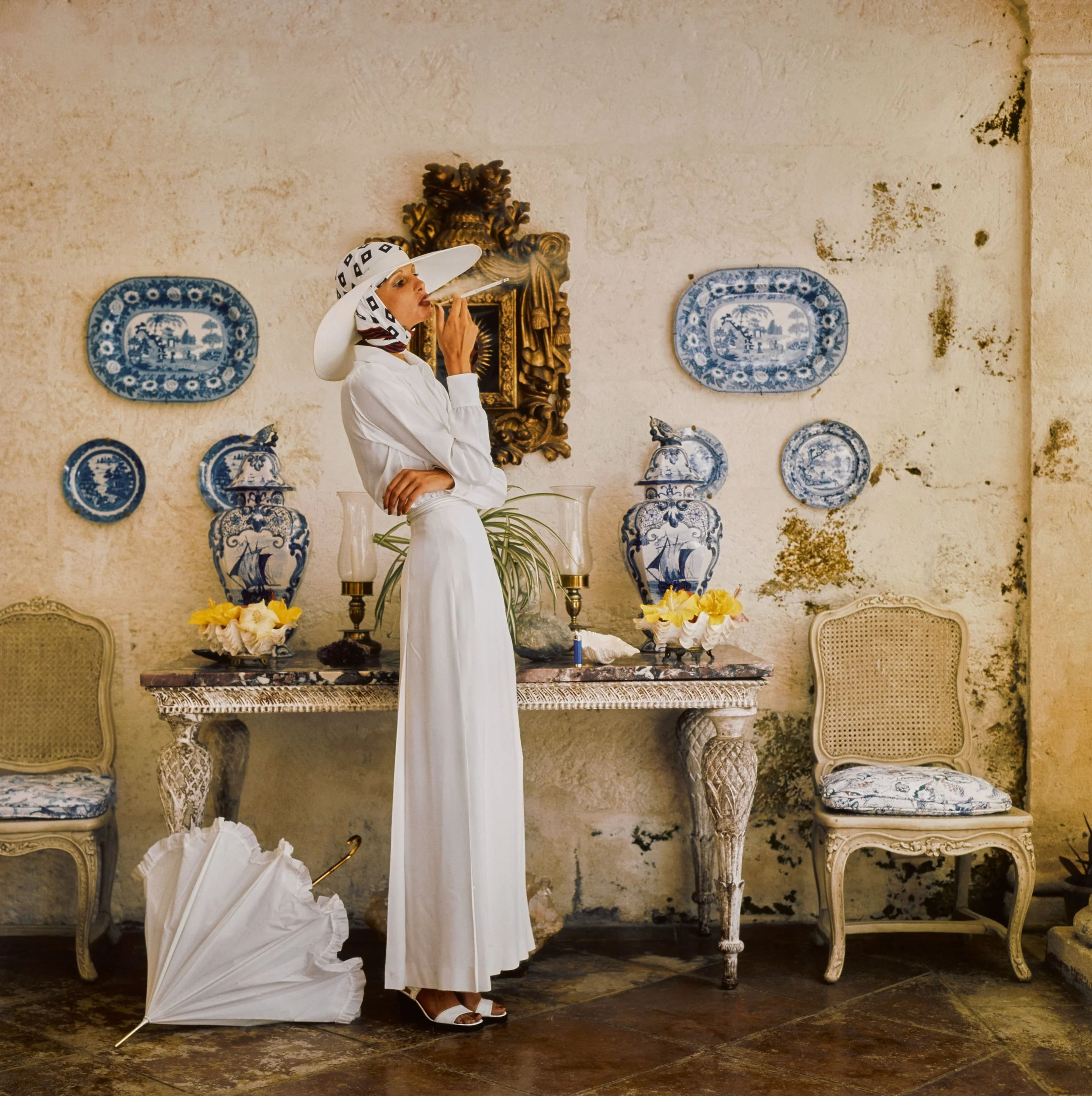 Throughout the 1970s, Norman Parkinson redefined fashion photography by embracing exotic landscapes and cinematic storytelling. Photographed for British Vogue in Barbados in 1973, this portrait of longtime muse Apollonia van Ravenstein reflects his s