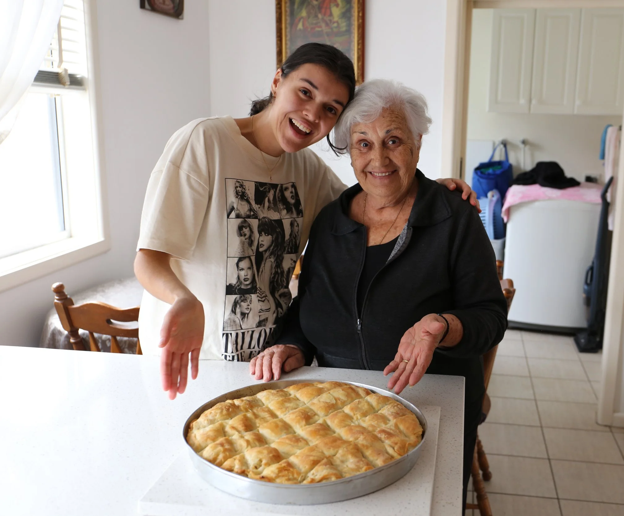 Three women smiling and enjoying together, one holding a slice of pizza in a cozy indoor setting with natural light.