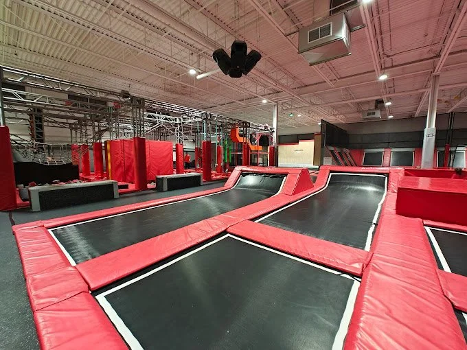 Indoor trampoline park with red and black trampolines, obstacle course, and padded structures.