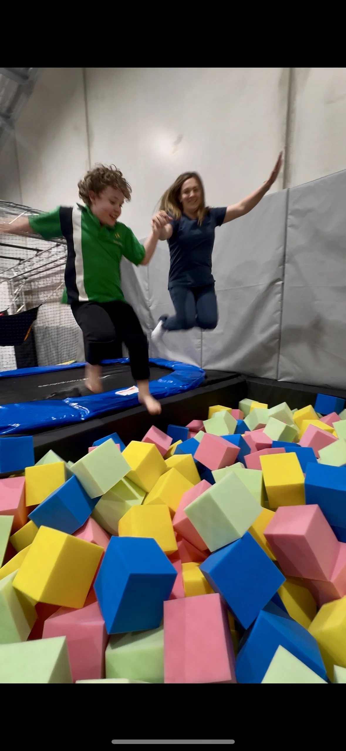 Child jumping on trampoline in indoor play area with colorful equipment.