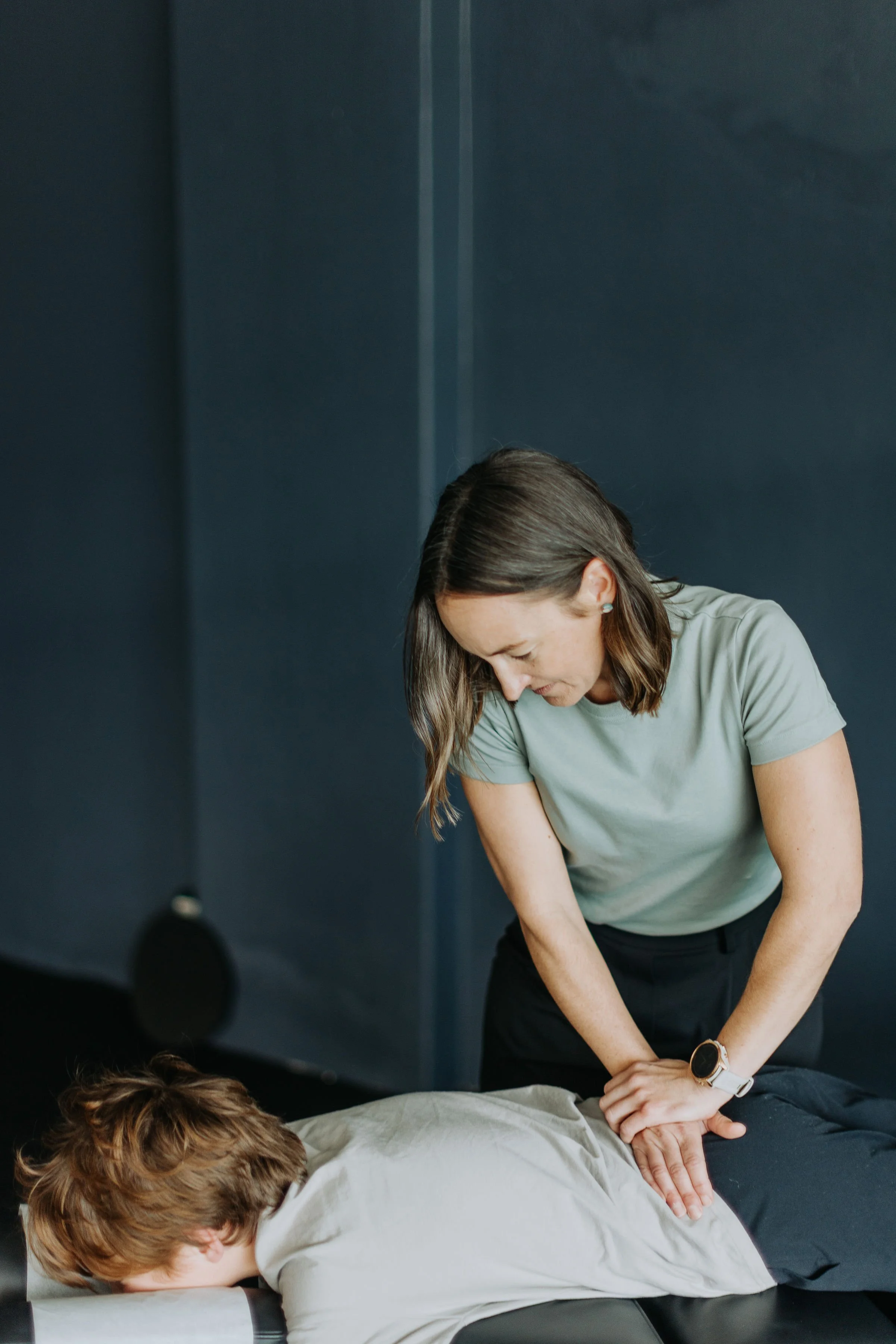 A woman performing CPR on a person lying face down on a table in a clinical setting.