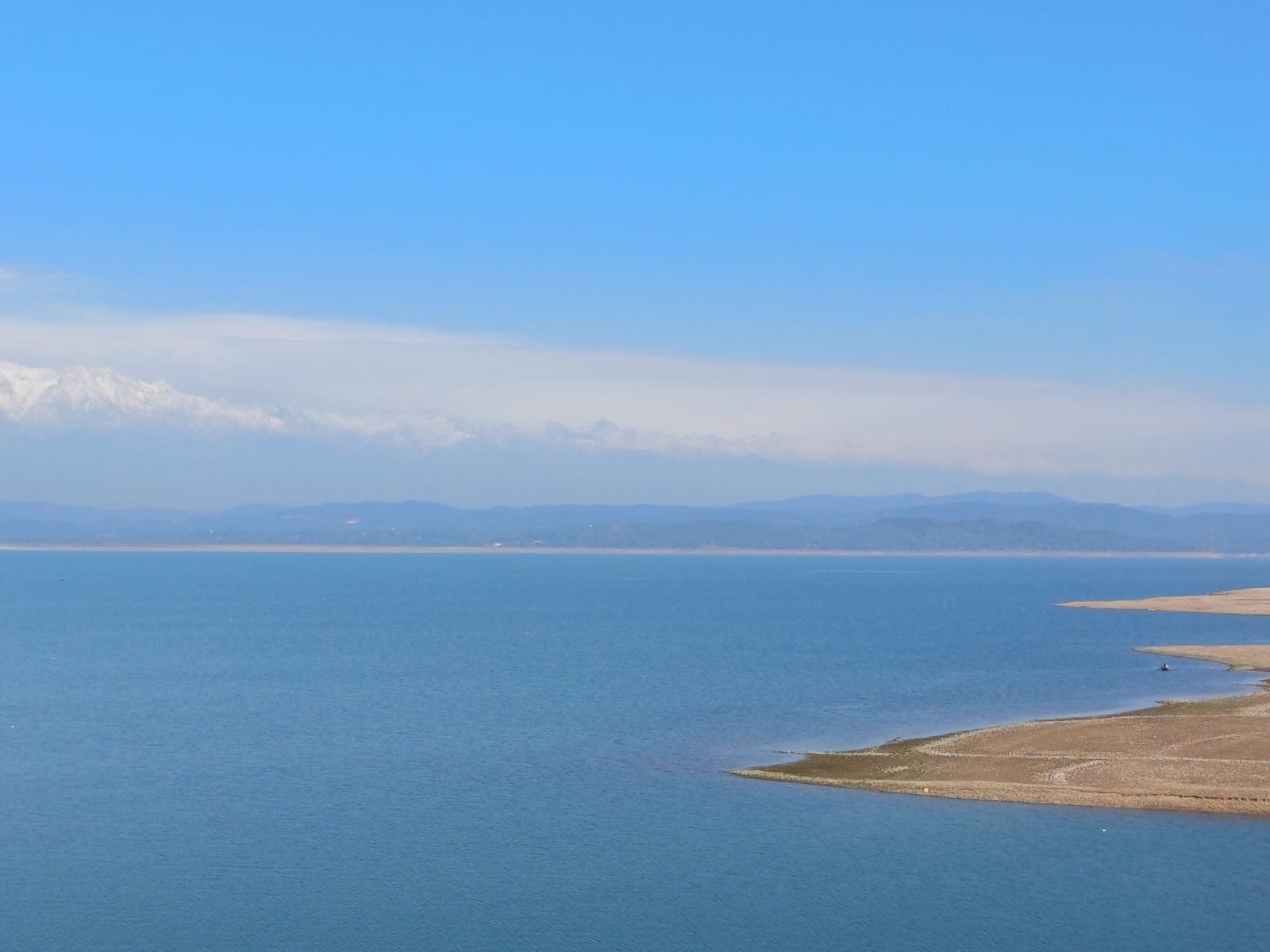 Landscape with a large blue lake and distant mountain range under a clear blue sky.