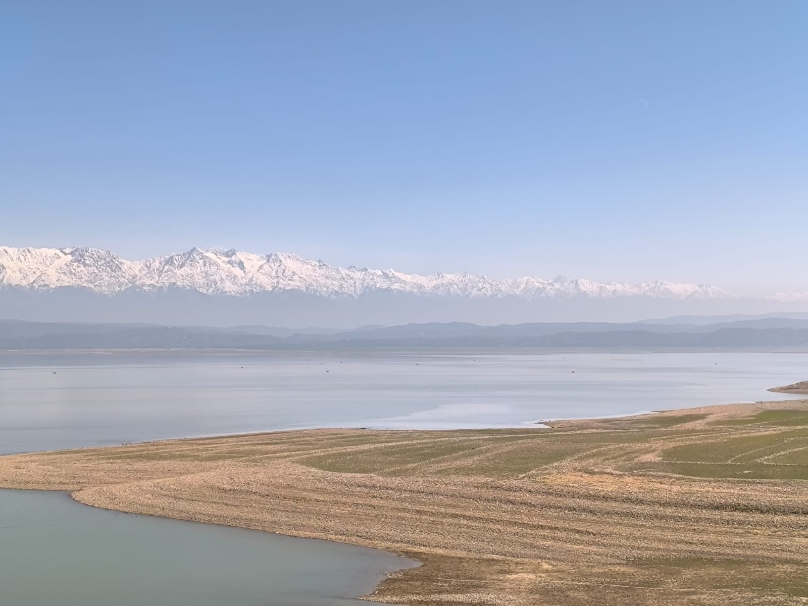 Scenic view of a vast lake with a snow-capped mountain range in the distance, under a clear blue sky.