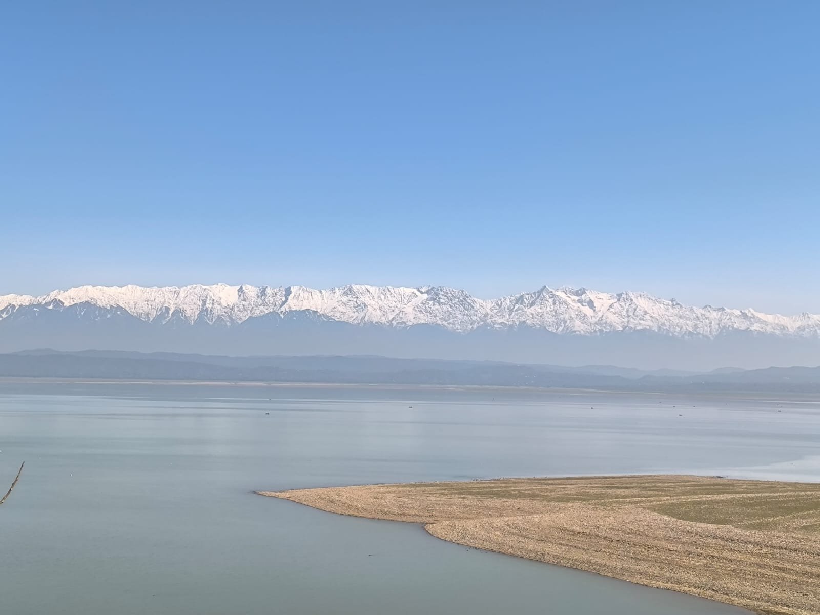 Snow-capped mountains reflected in a large body of water under a clear blue sky.