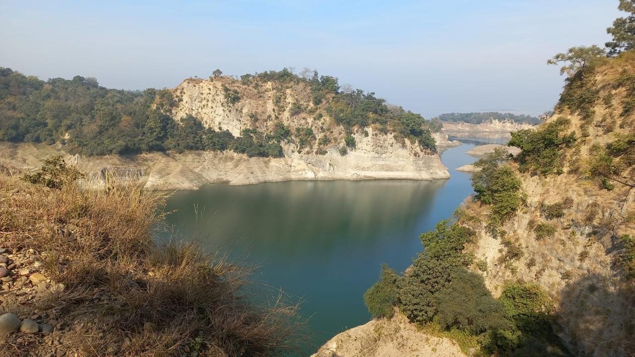 Scenic view of a calm river surrounded by rocky cliffs and lush greenery, under a clear blue sky.