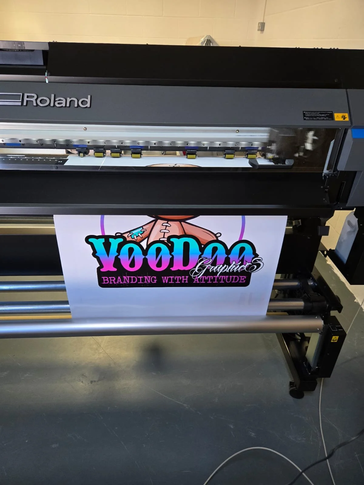 A large Roland printer printing a colorful banner with the text 'YooDaa Graphics' and 'Branding with Attitude'.