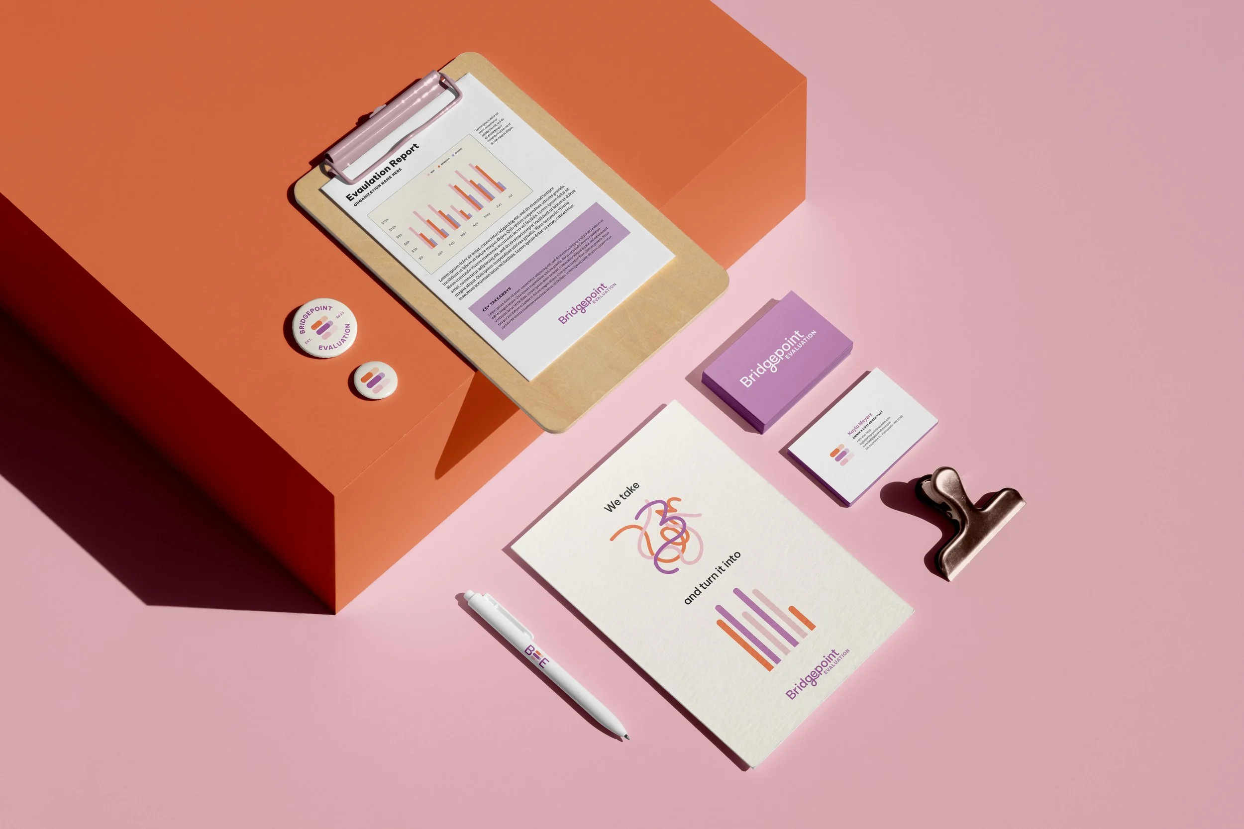 Stationery and branding set on a pink background, including a clipboard with a report, business cards, a badge, a pen, and a binder clip.