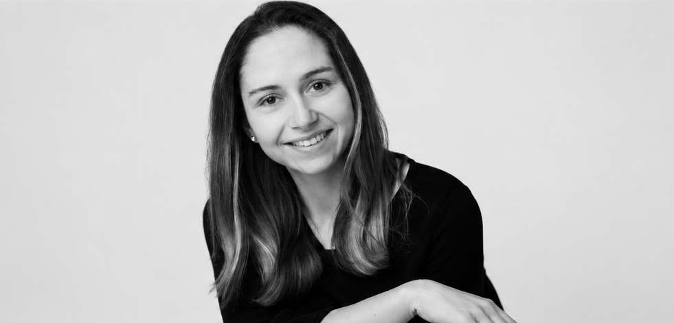 Portrait d'une femme souriante avec des cheveux longs et bruns, portant un haut noir, sur un fond blanc.