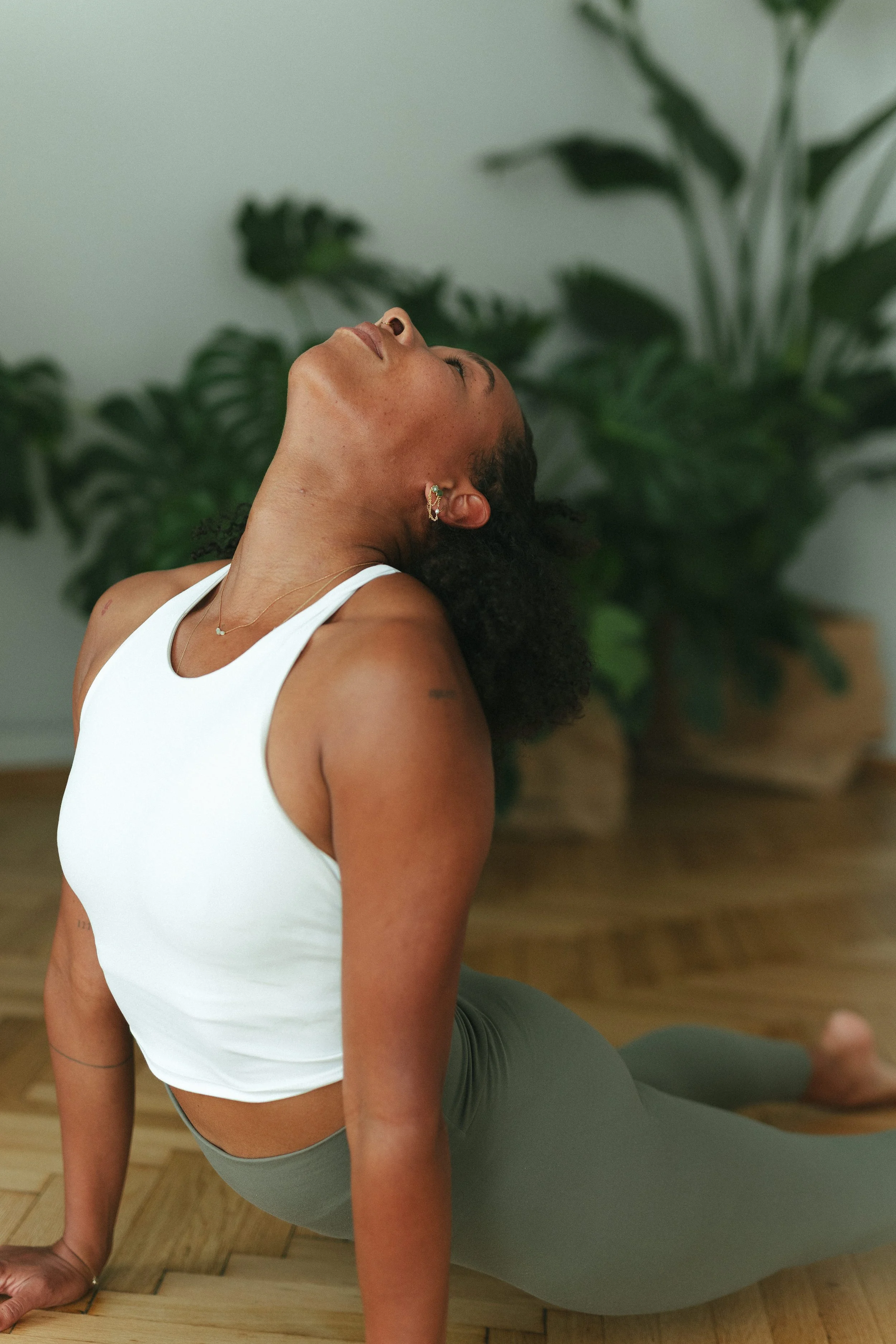 Frau macht Yoga auf Holzboden vor grünen Zimmerpflanzen.