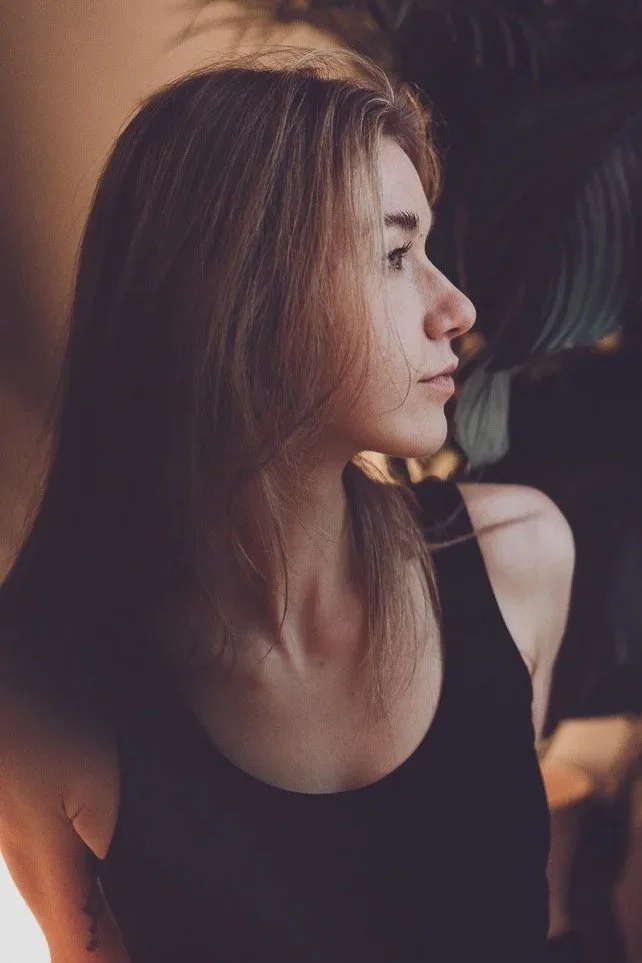 Seitenprofil eines jungen Frau mit braunen Haaren in einem schwarzen Top, vor dunklem Hintergrund.