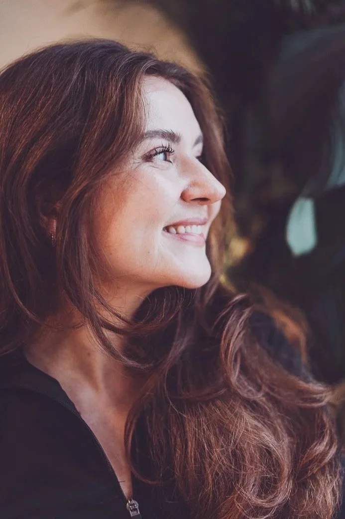 Nahaufnahme einer lachenden Frau mit braunen, lockigen Haaren, die nach rechts blickt.