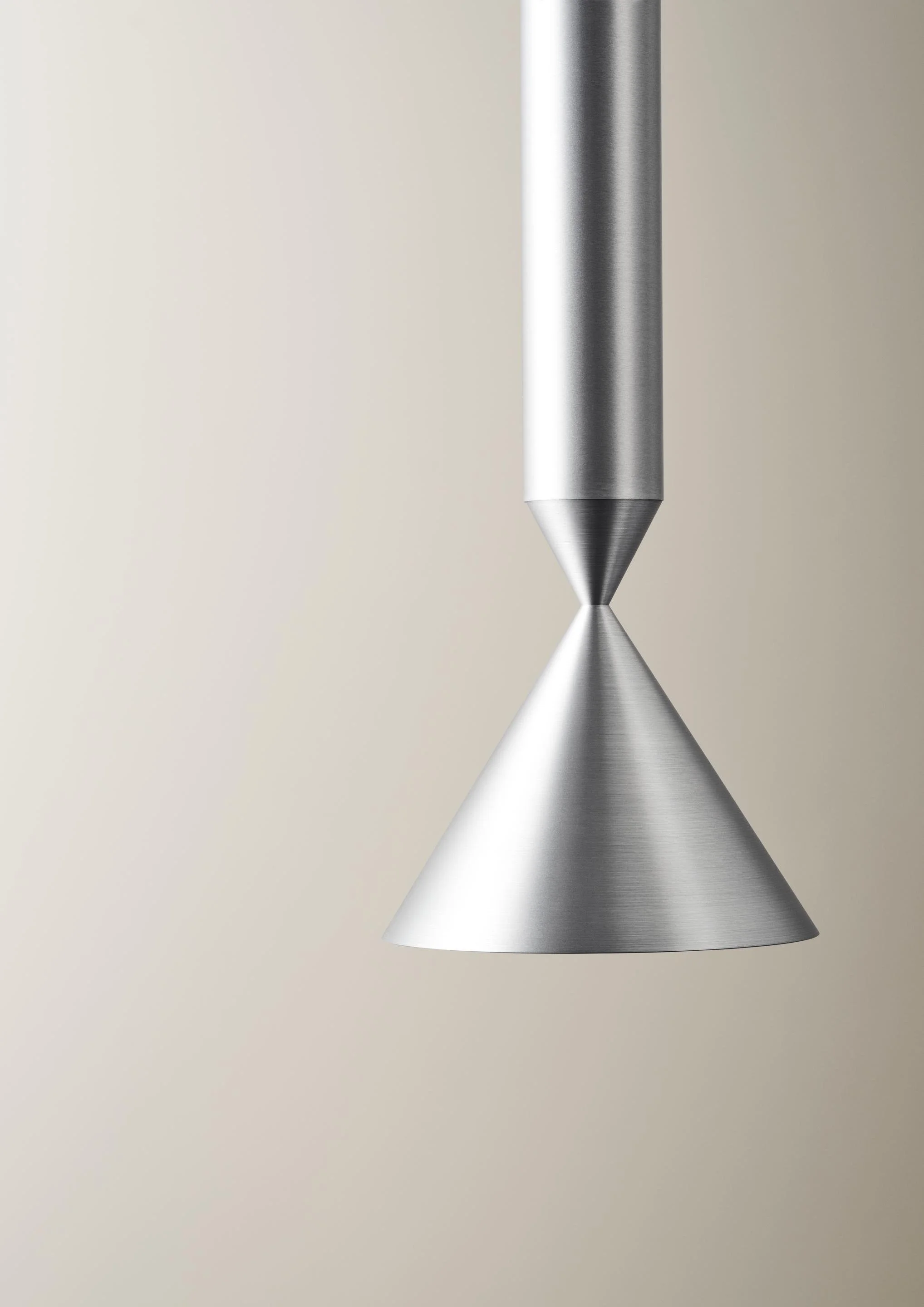 Close-up of a modern, metallic, cone-shaped pendant light against a plain, off-white background.
