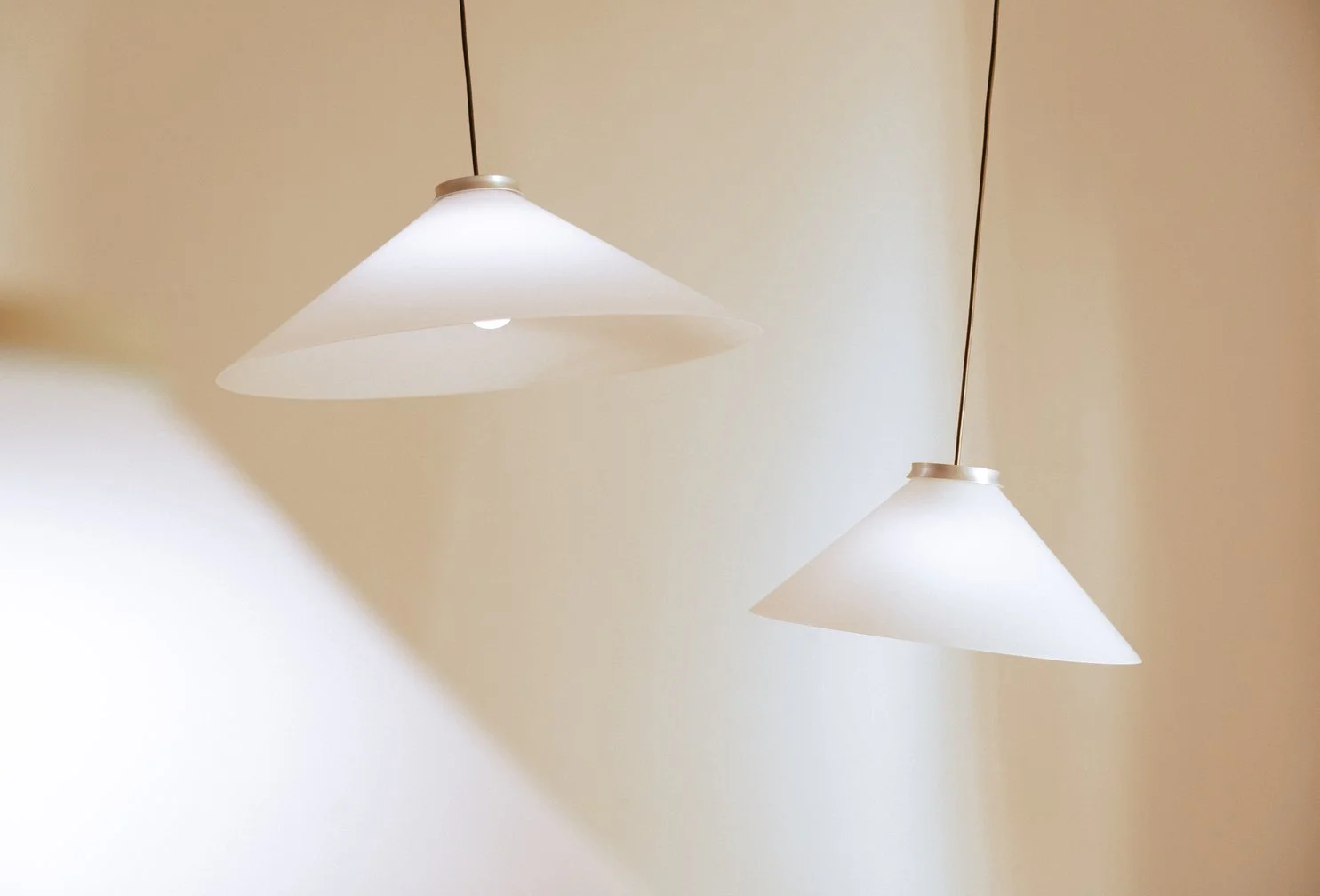 Two white cone-shaped pendant lights hanging from cords against a beige ceiling.