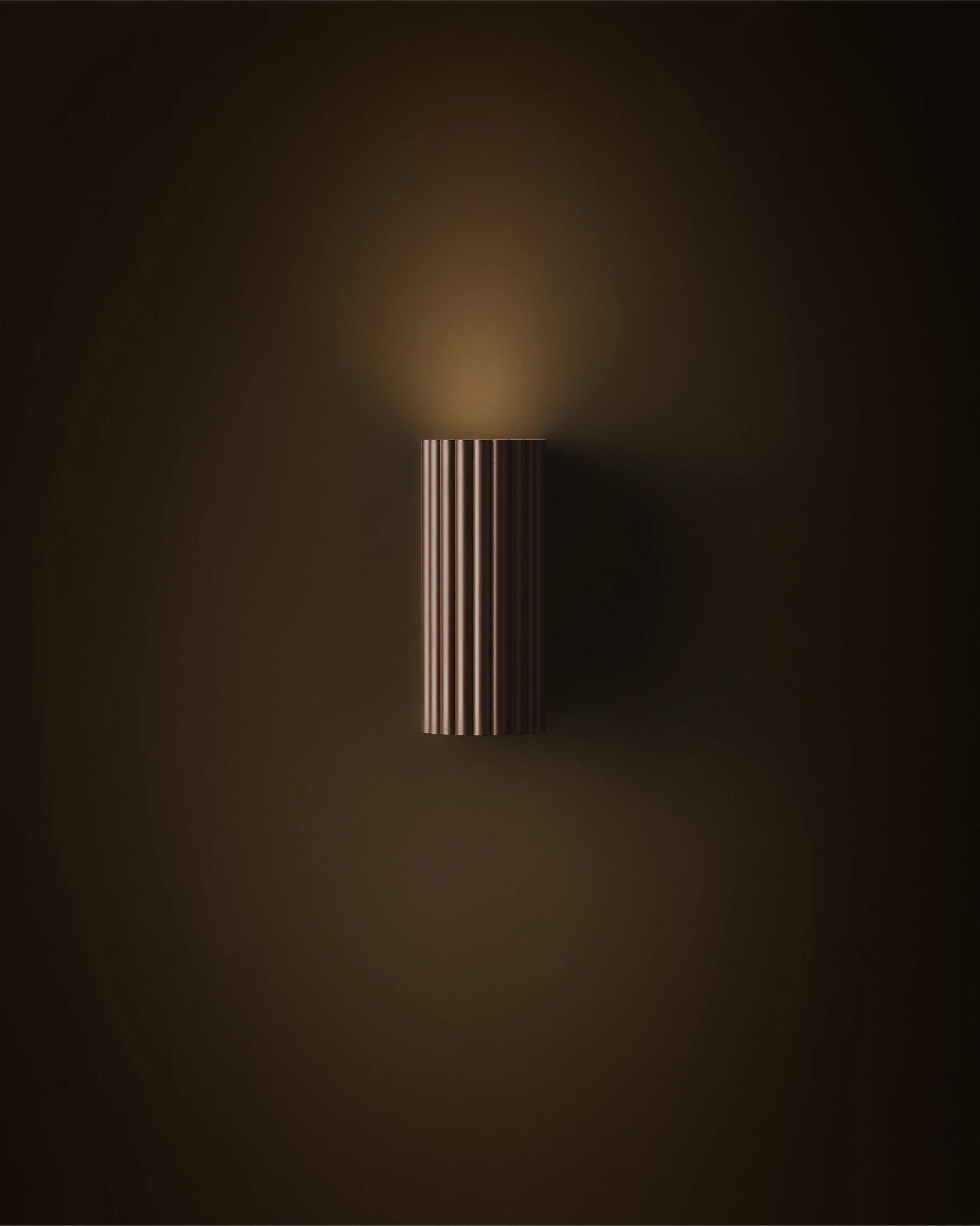 A vertical, brown, ribbed wall sconce casting a soft glow on a dark wall.