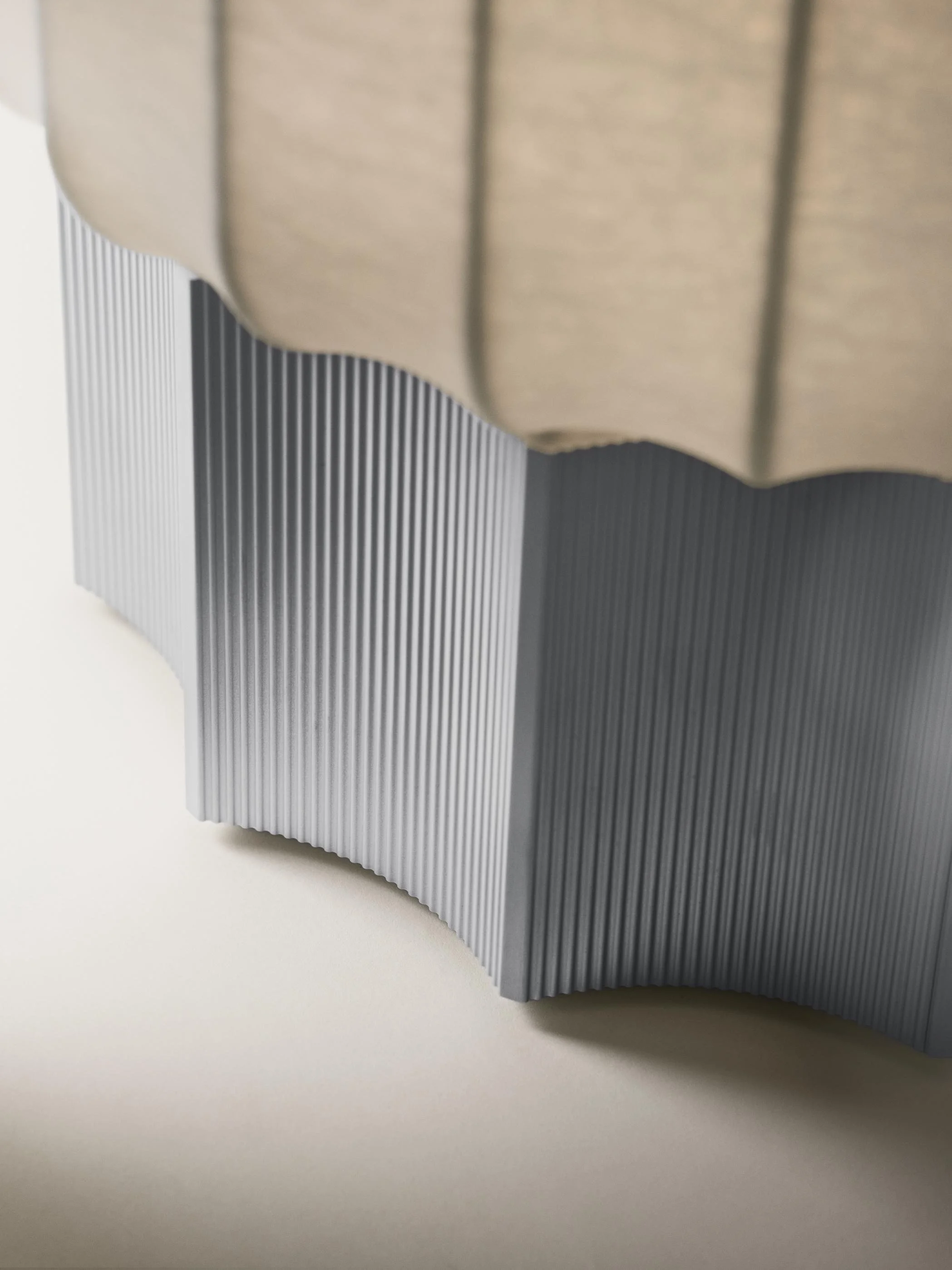 Close-up of a modern, curved, metallic architectural structure with vertical ridges, placed on a smooth, light-colored surface.