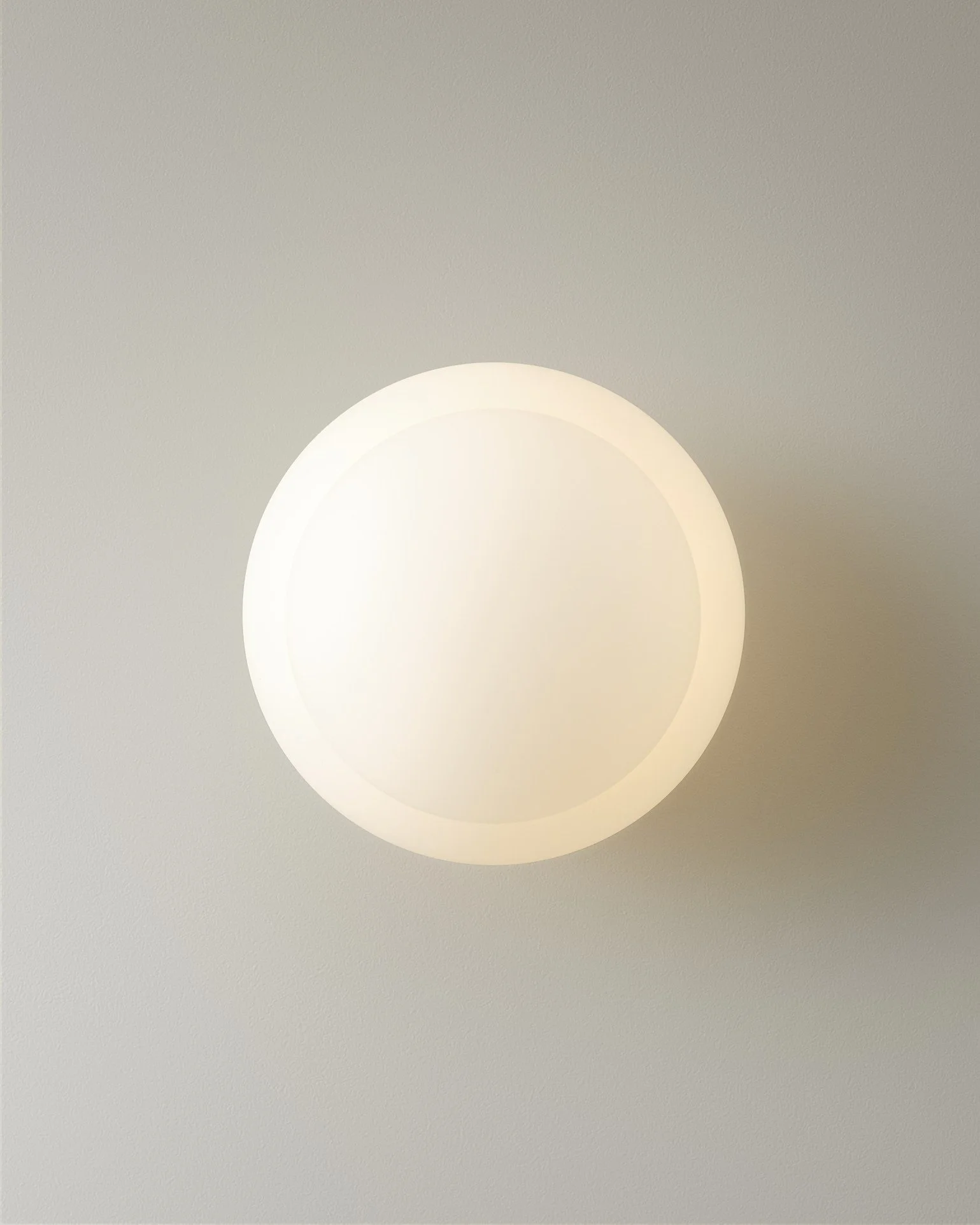 A circular, glowing wall sconce light fixture on a plain wall.