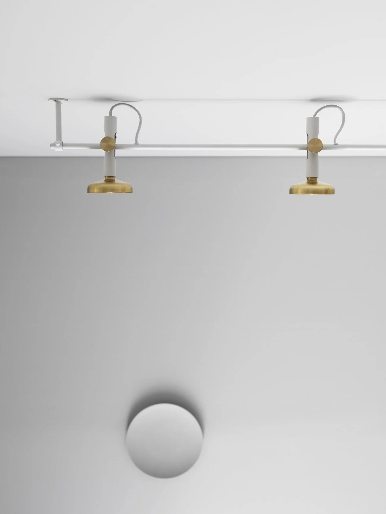 Modern ceiling light fixture with two adjustable brass and white spotlights mounted on a white ceiling.