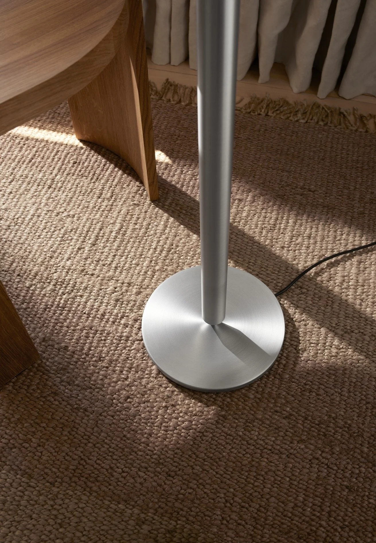 Close-up of a modern silver floor lamp with a round base on a textured beige carpet.