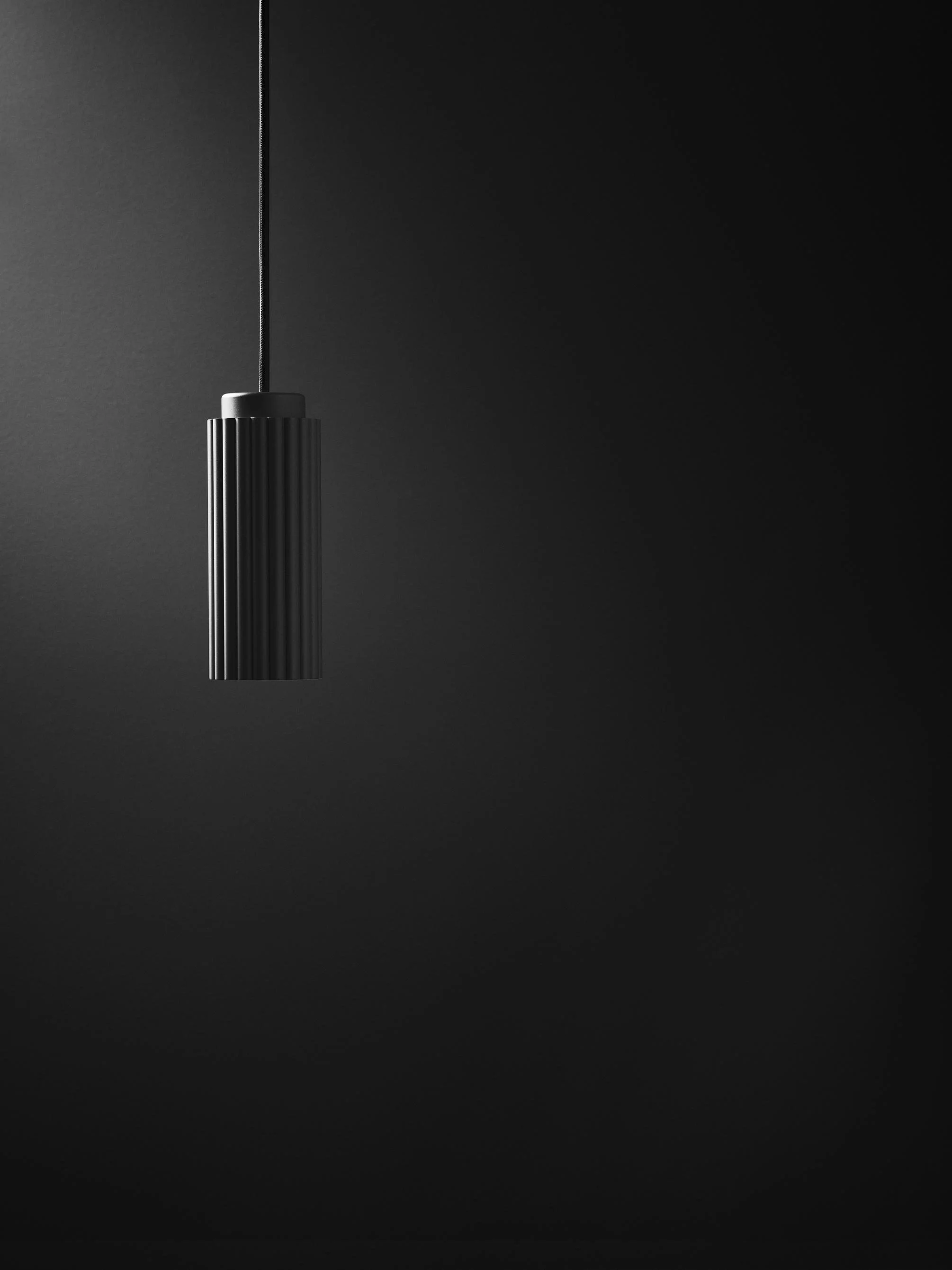 Black pendant light hanging against a dark wall.