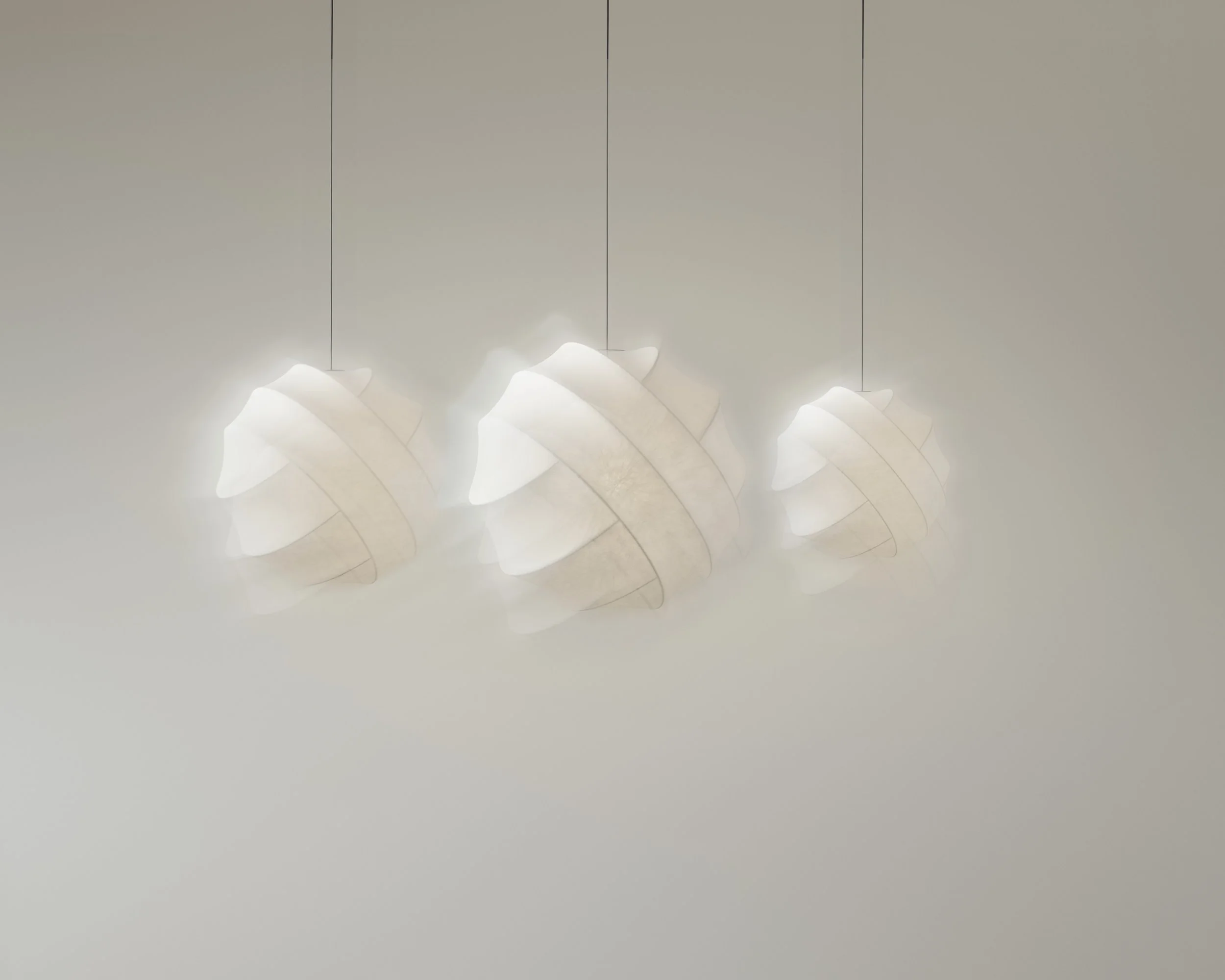 Three contemporary pendant lights with white, curved, layered shades hanging from thin cords in a minimalist setting.