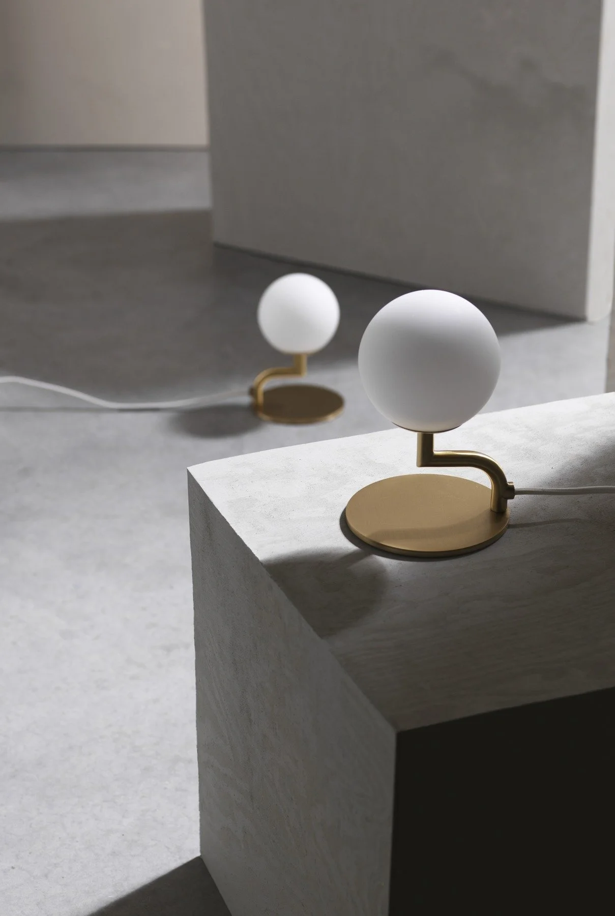 Two modern table lamps with round white globes and gold bases on light-colored surfaces.