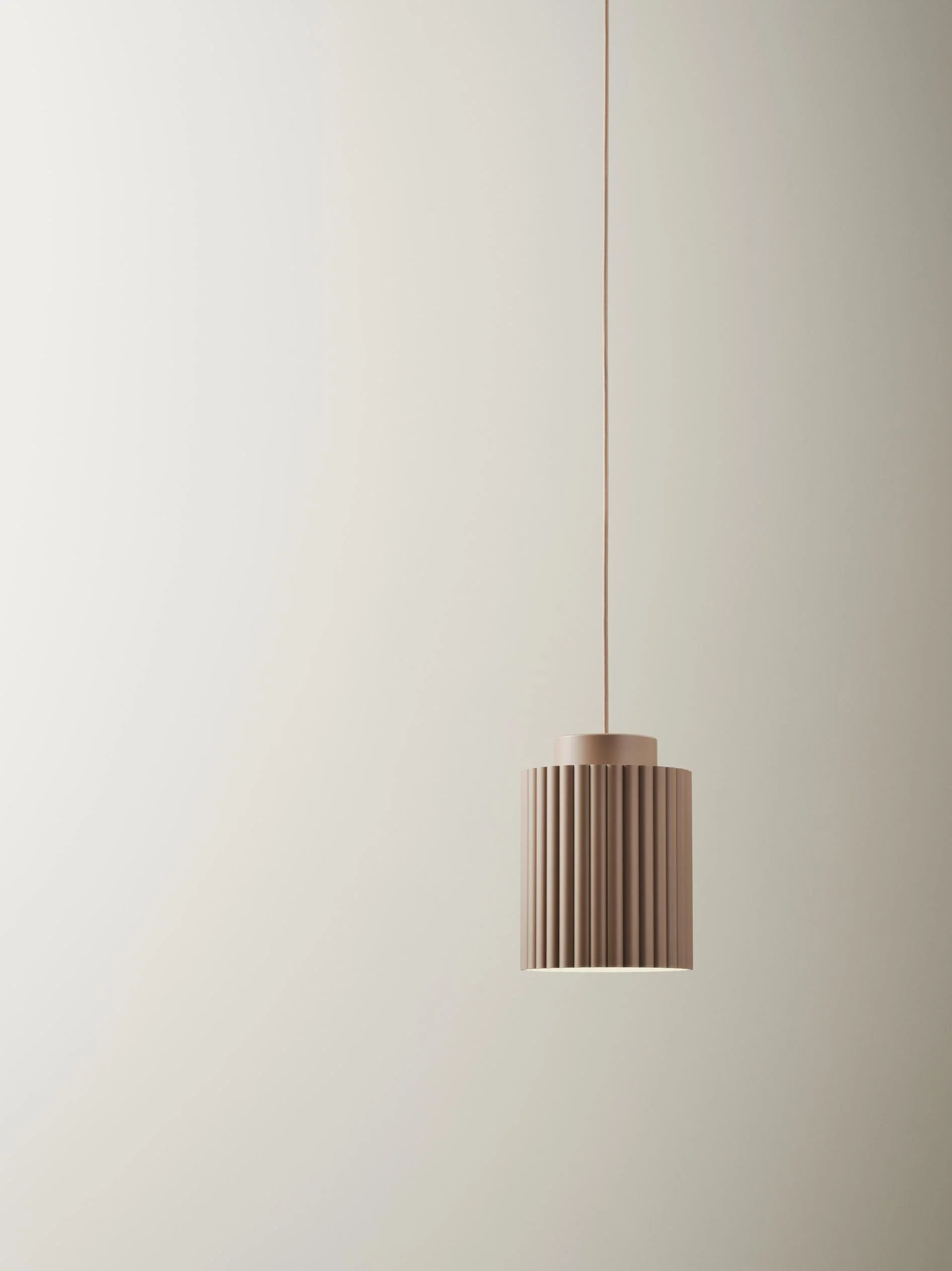 Minimalist beige pendant lamp with vertical ridges hanging from a beige cord in a light-colored room