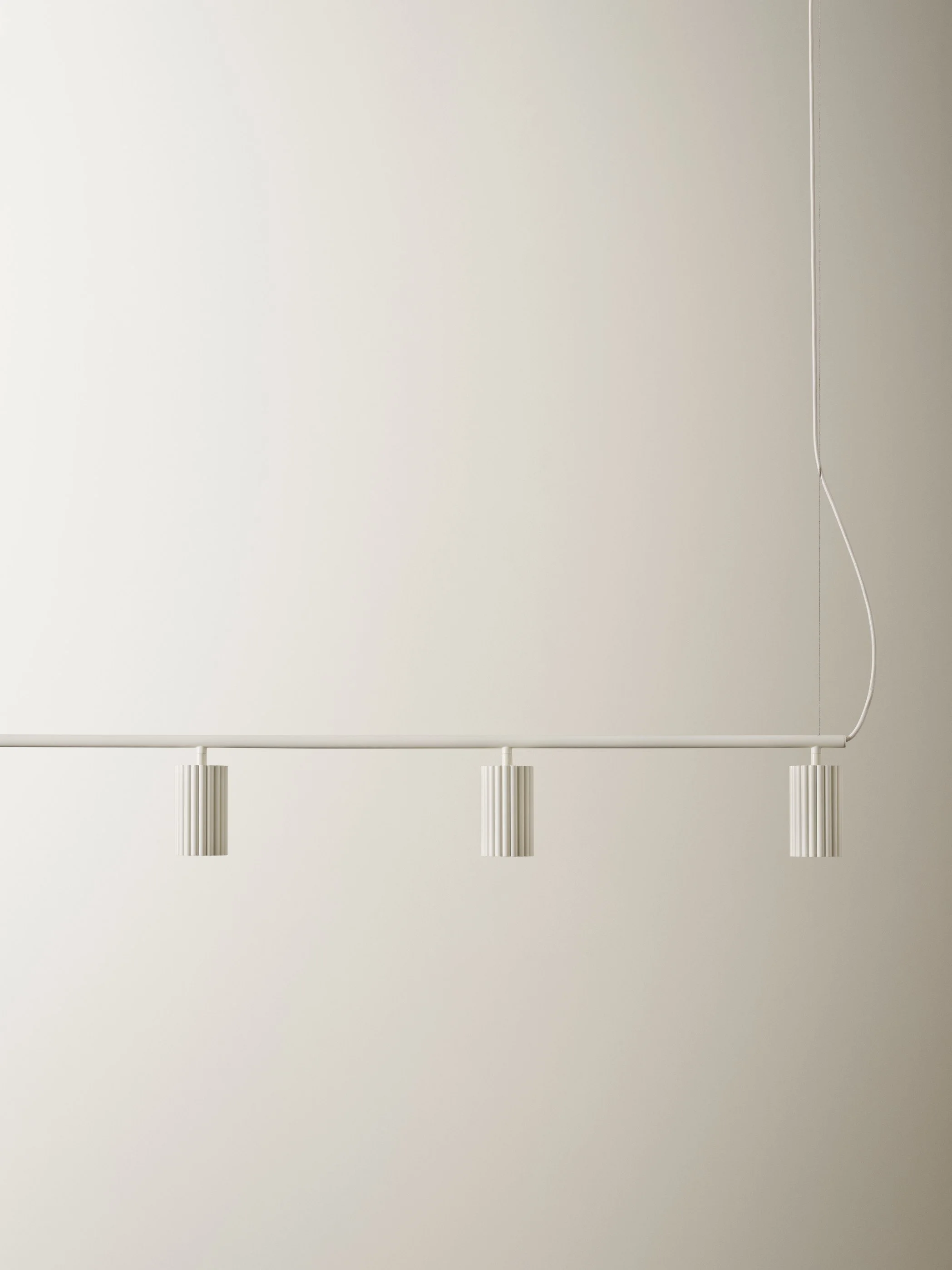 Minimalist white ceiling light fixture with three small, cylindrical, ribbed lamps hanging from a straight white rod against a plain wall.