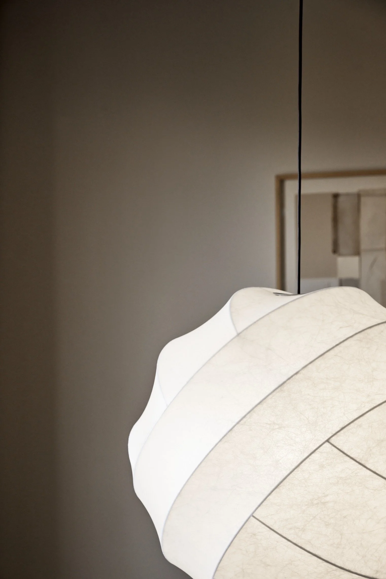 Close-up of a modern hanging lamp with a wavy white shade in a dimly lit room.