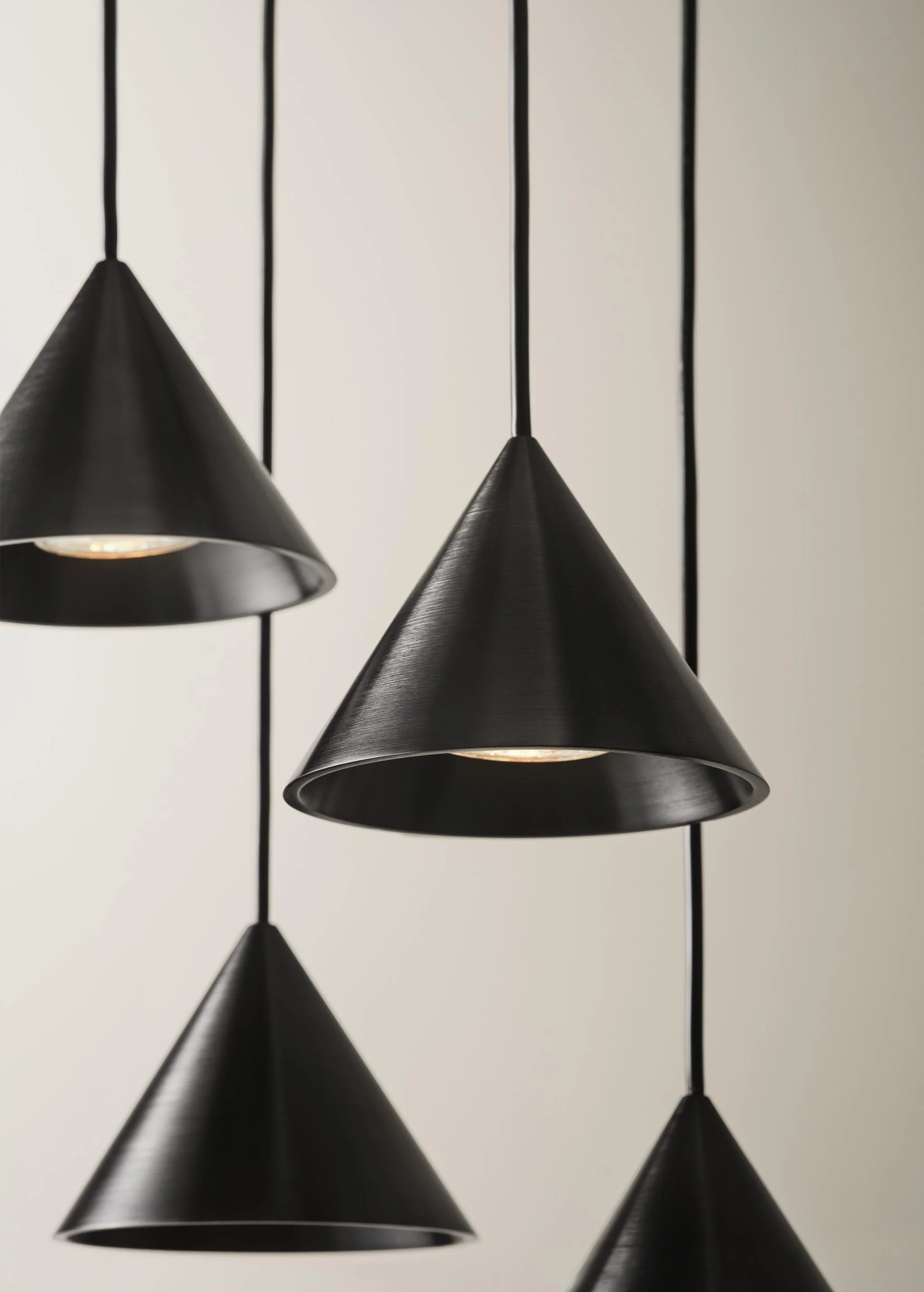Three black cone-shaped pendant lights hanging from the ceiling against a white background.