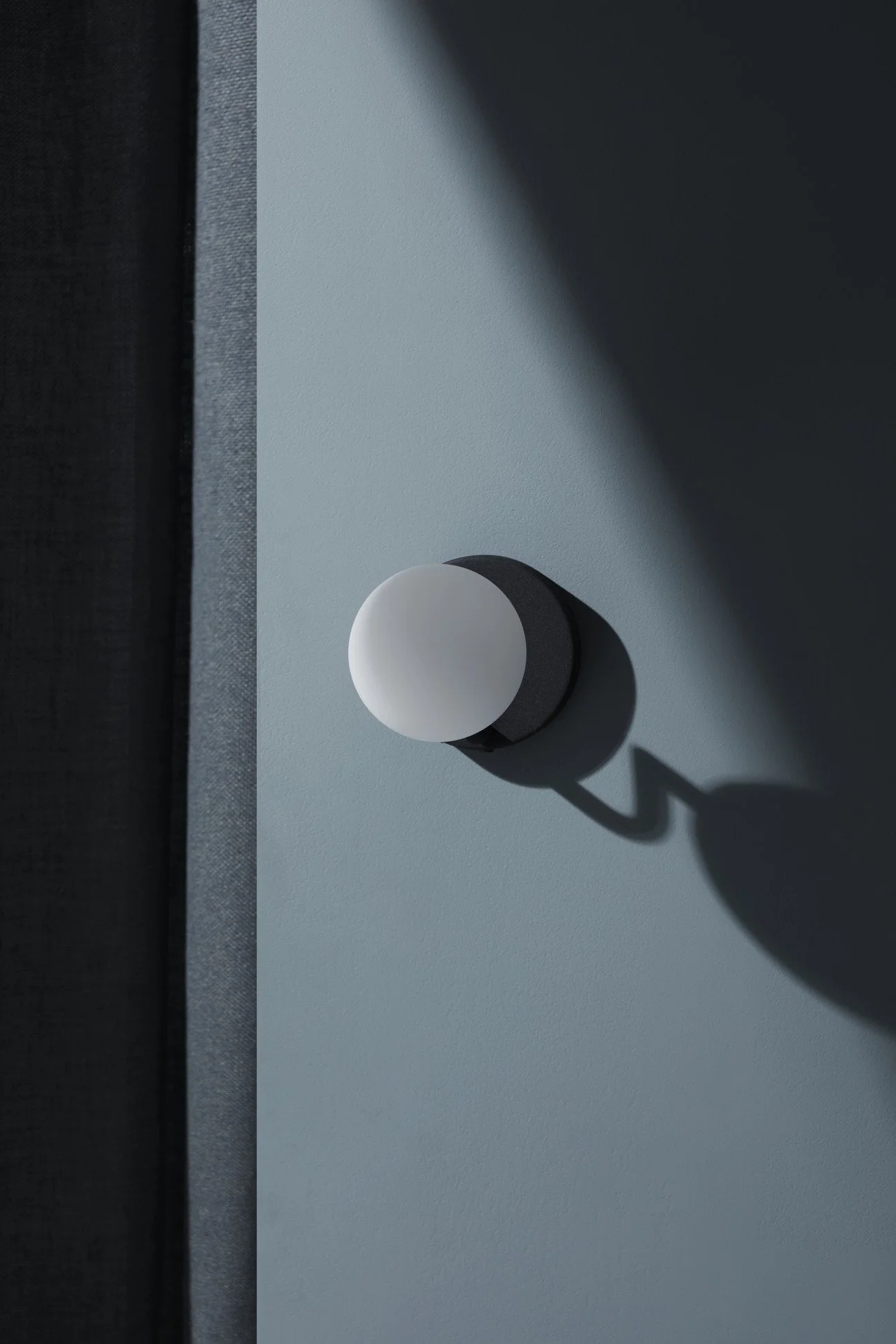 Close-up of a modern wall-mounted light fixture casting a shadow on a light blue wall.