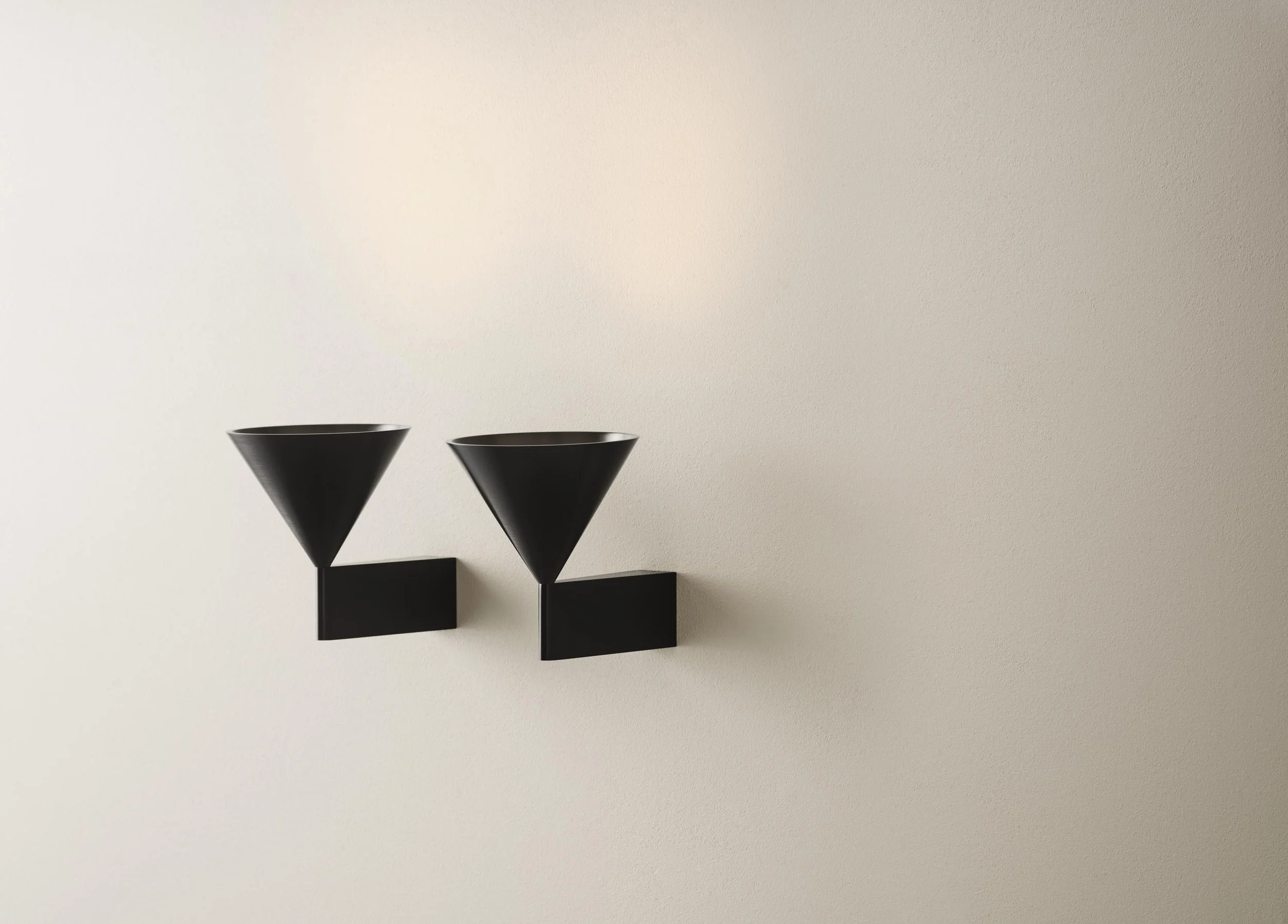 Two black wall-mounted light fixtures with cone-shaped shades on a plain, off-white wall.