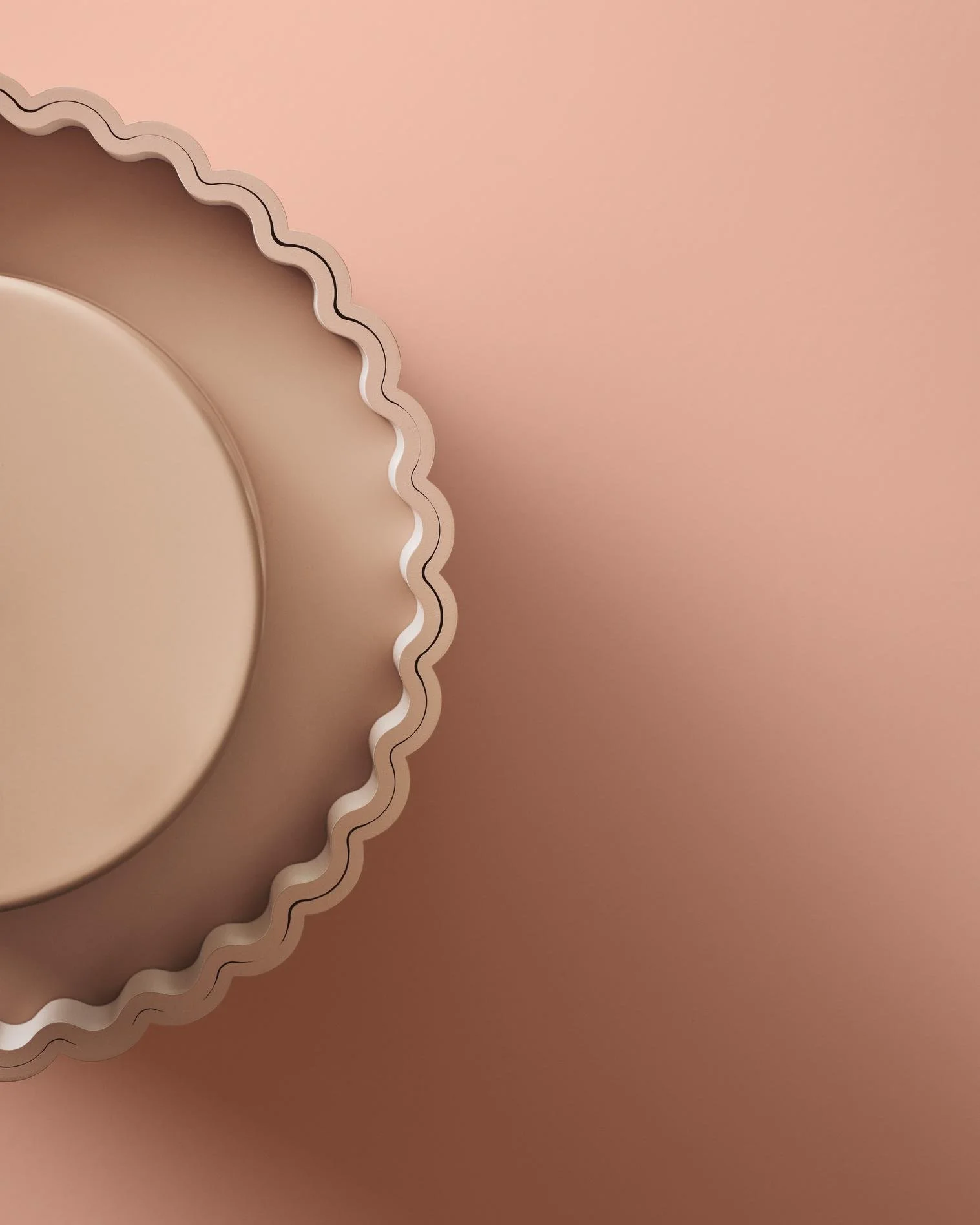 Close-up of a round, beige tart mold with a ruffled edge, placed on a pink surface.