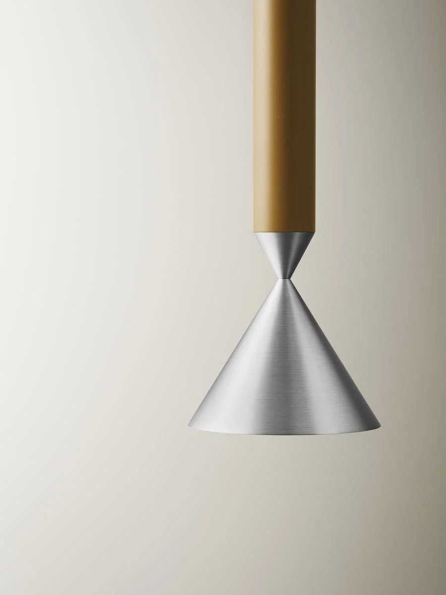 Close-up of a modern pendant light with a conical metallic shade and a gold-colored cylindrical fixture against a plain light background.