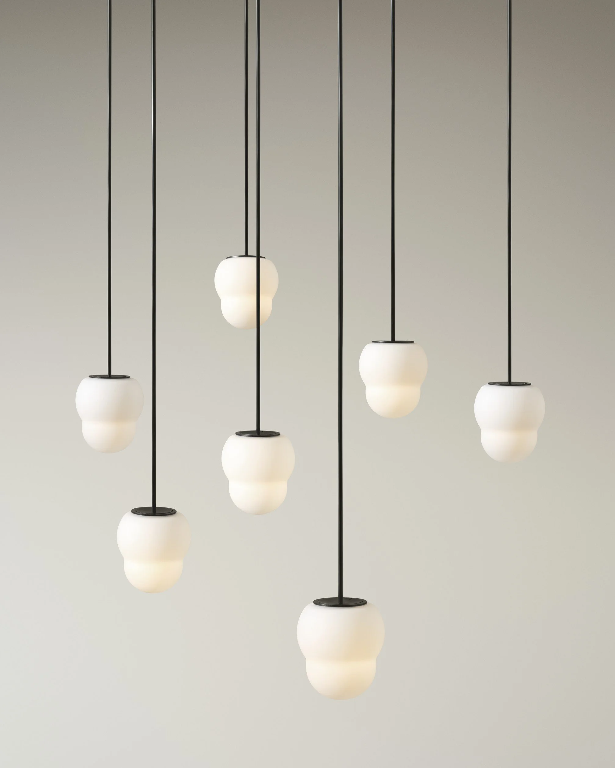 Modern pendant lights with white glass shades hanging from black cords against a plain gray wall.