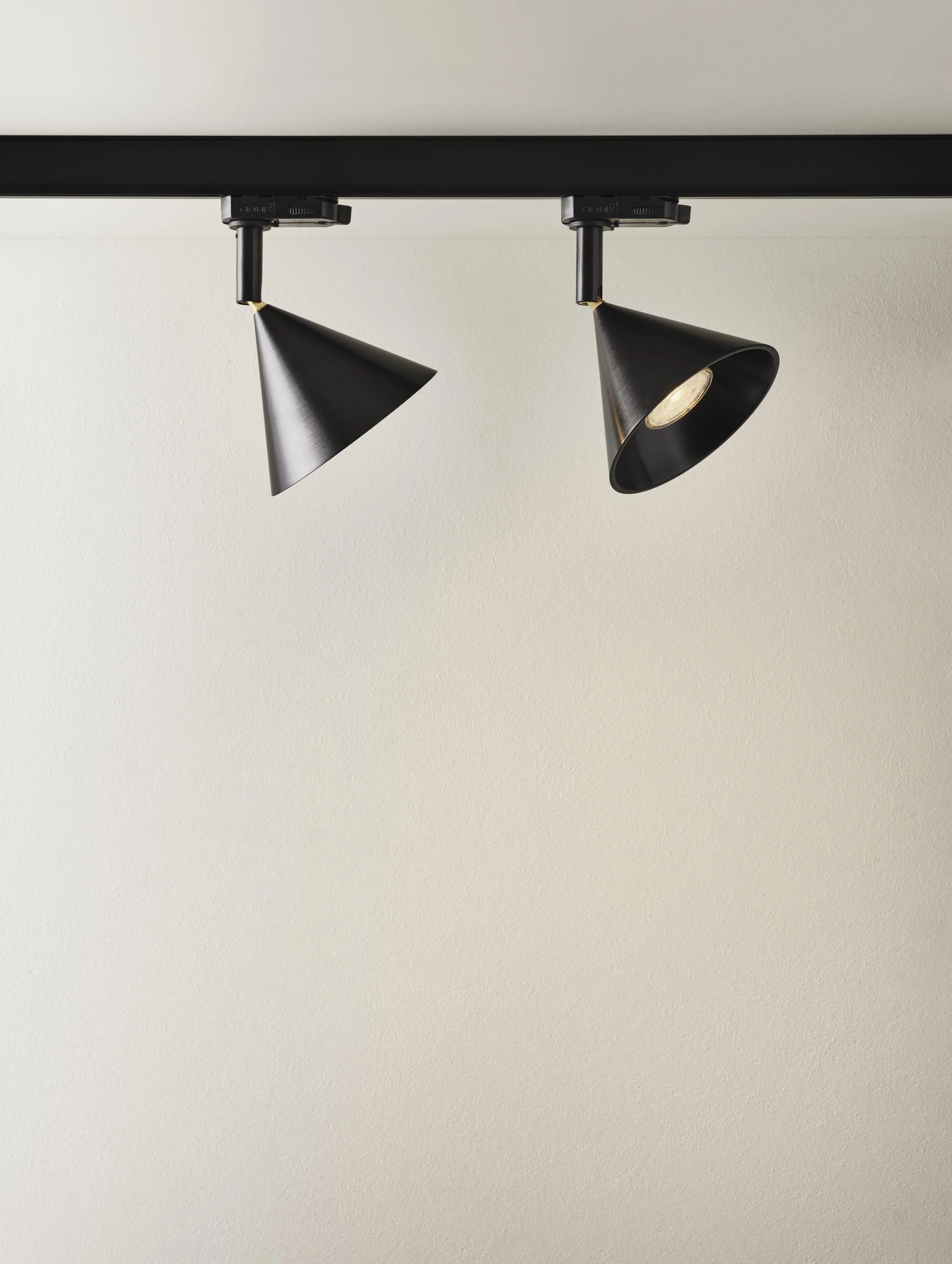 Two black adjustable track lights mounted on a ceiling, with one light turned on.