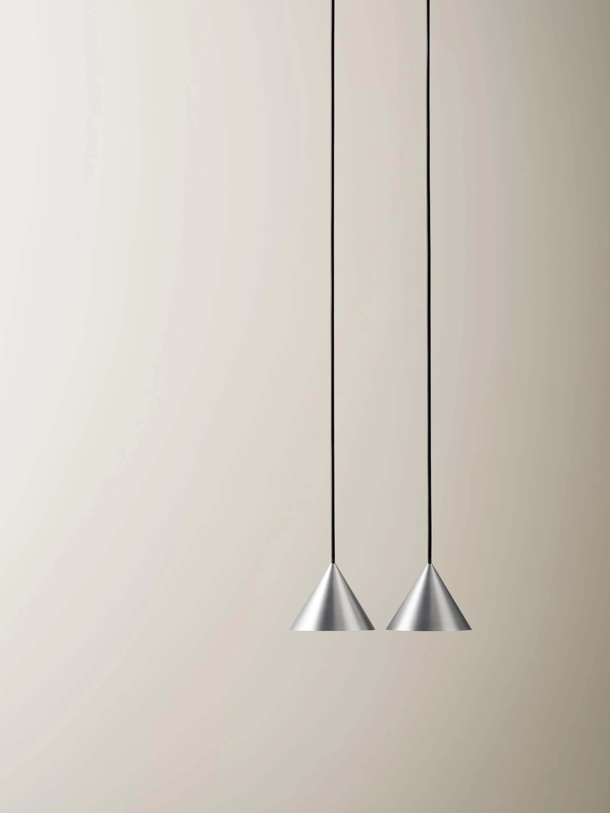 Two modern silver cone-shaped pendant lights hanging from black cords against a plain beige wall.
