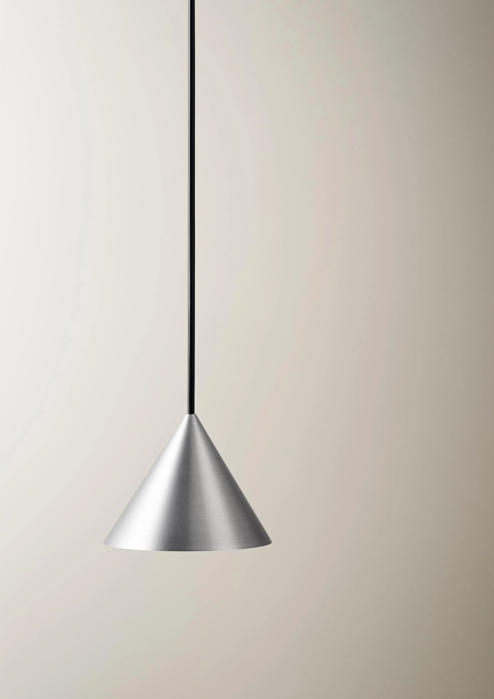 Minimalist hanging pendant lamp with a metallic cone shade, suspended by a black cord against a plain beige wall.