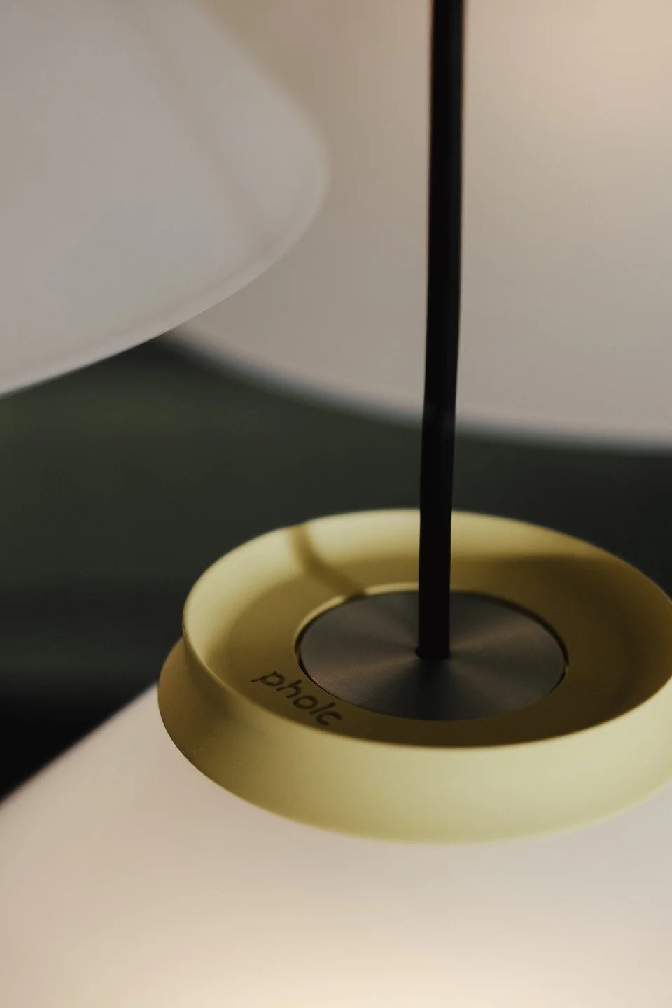 Close-up photo of a candle with a black wick, encircled by a beige holder labeled 'phic', against a background of abstract shapes and muted colors.