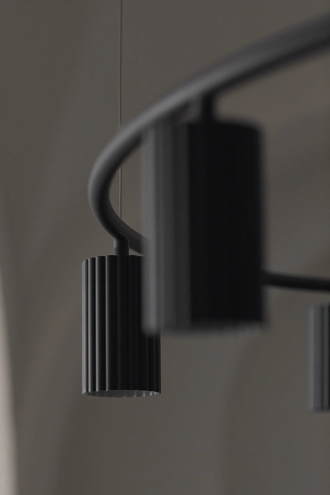 Close-up of modern black pendant lights with ribbed cylindrical design hanging from the ceiling in a minimalist interior.