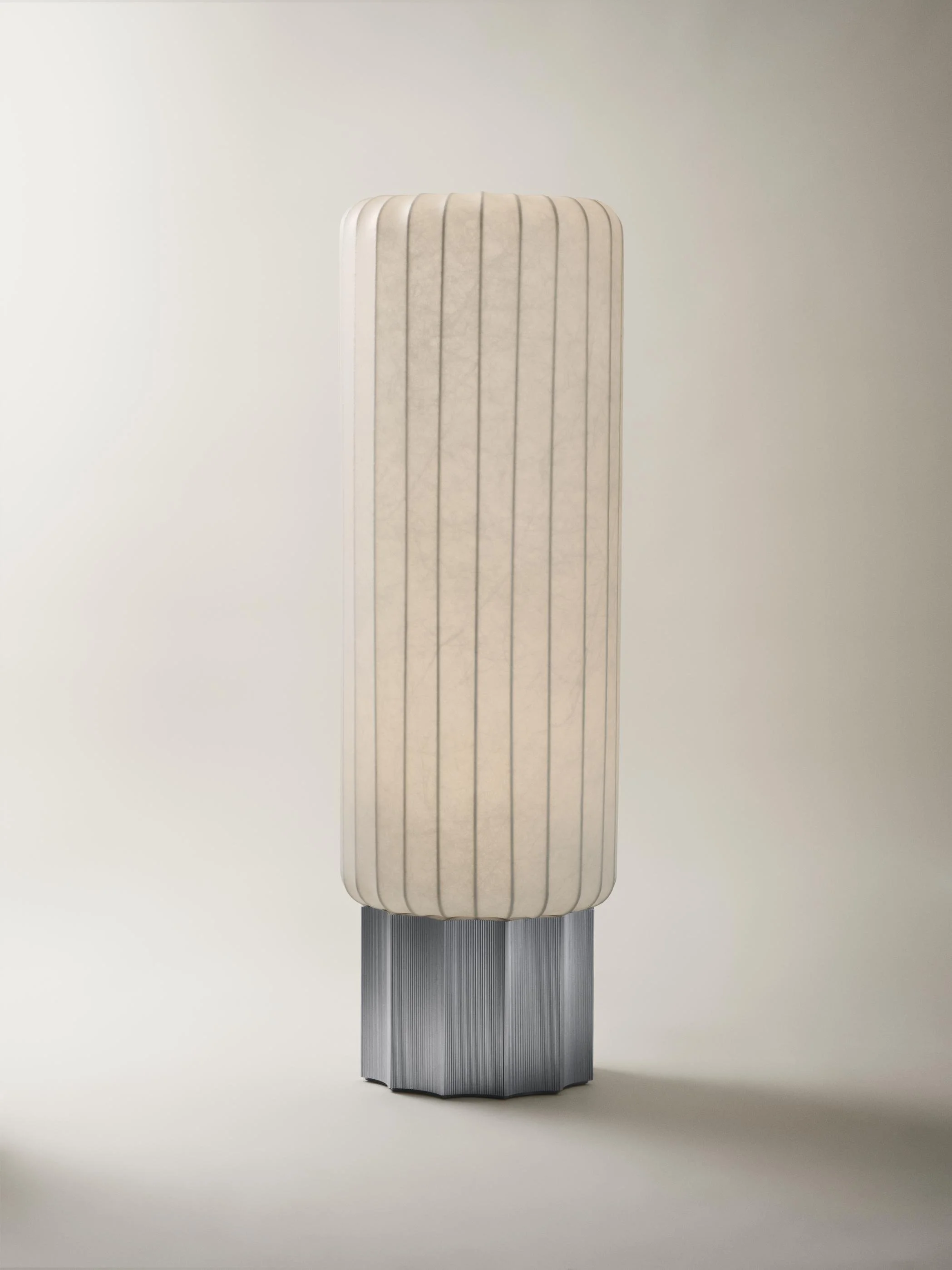 A tall, modern lamp with a pleated fabric shade and a geometric metallic base.