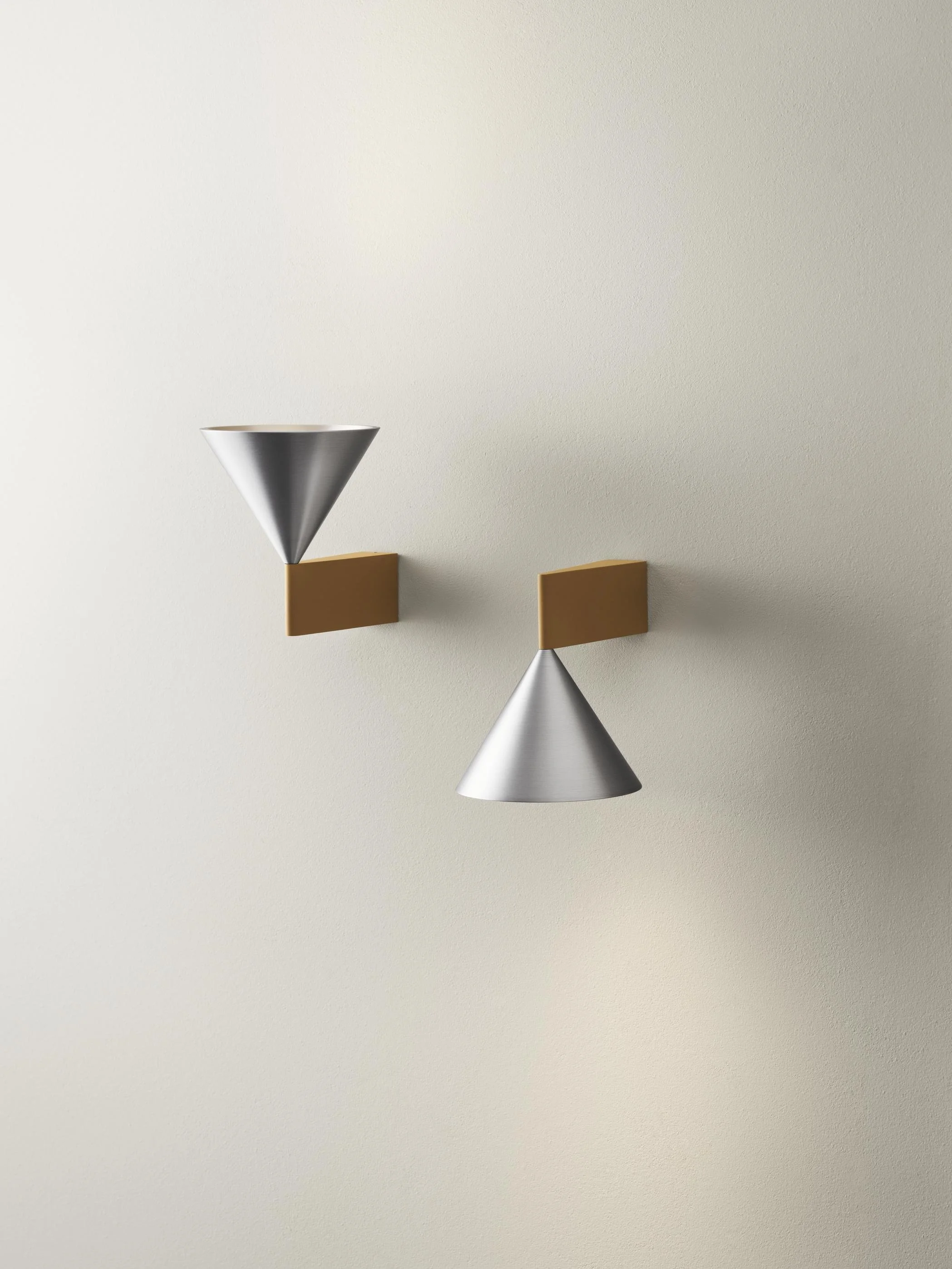 Modern wall-mounted light fixtures with metallic cone-shaped shades and rectangular brown bases against a plain cream-colored wall.