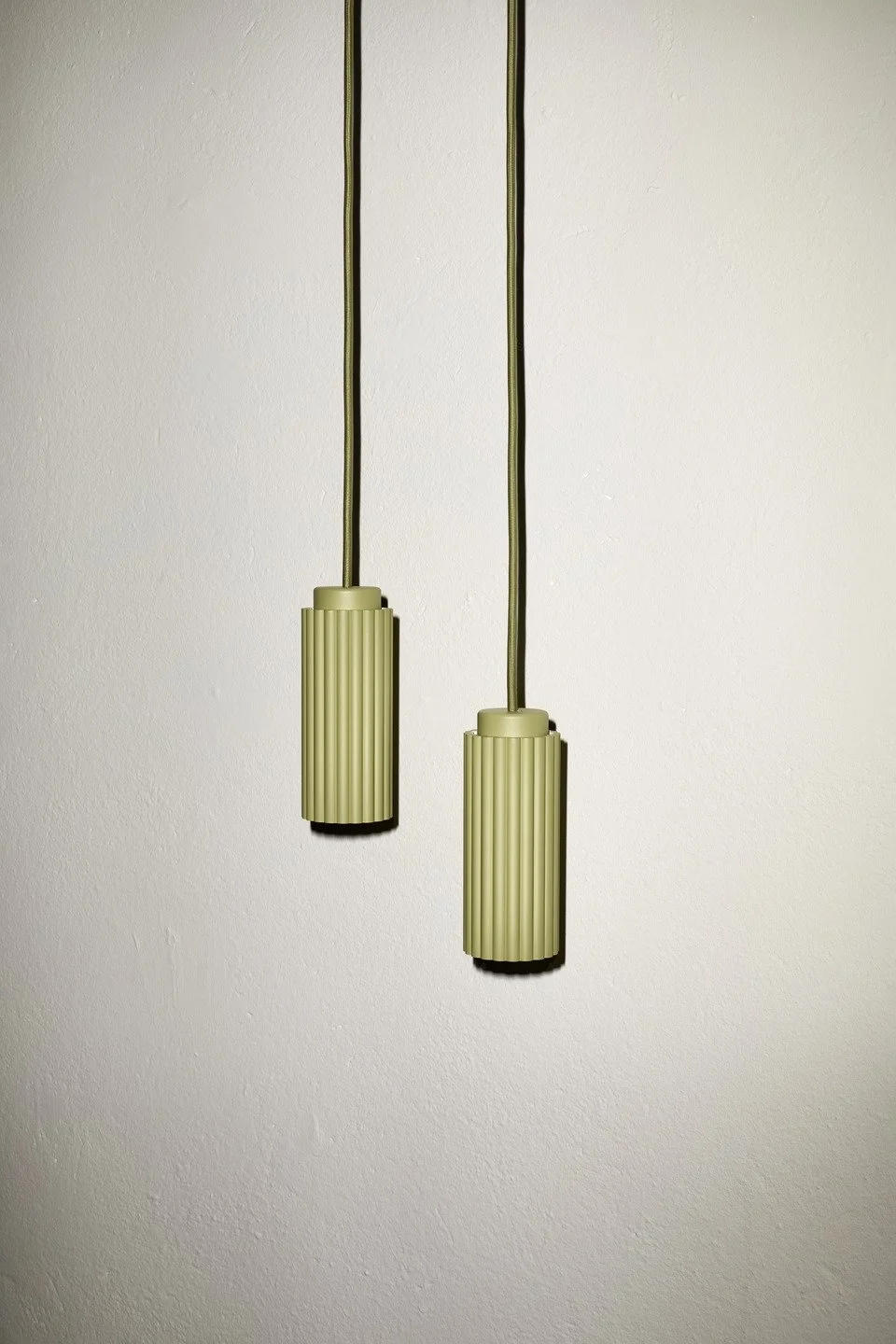 Two hanging beige pendant lights with ribbed texture against a plain white wall.