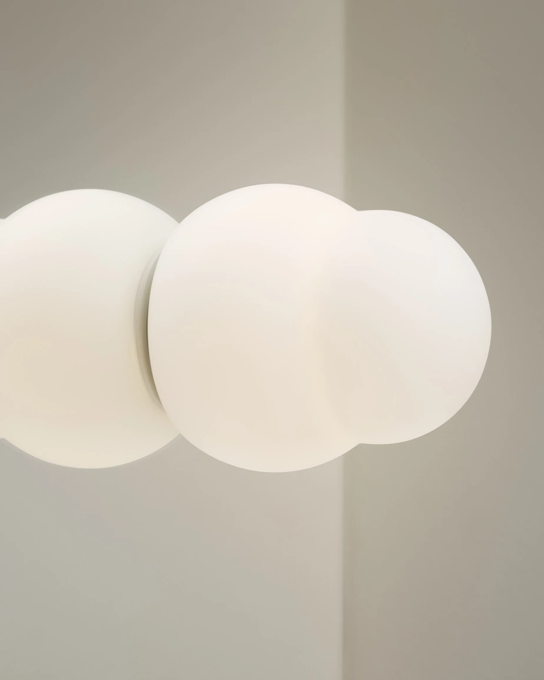 Close-up of a modern ceiling light fixture with three frosted white globes on a white ceiling and wall.