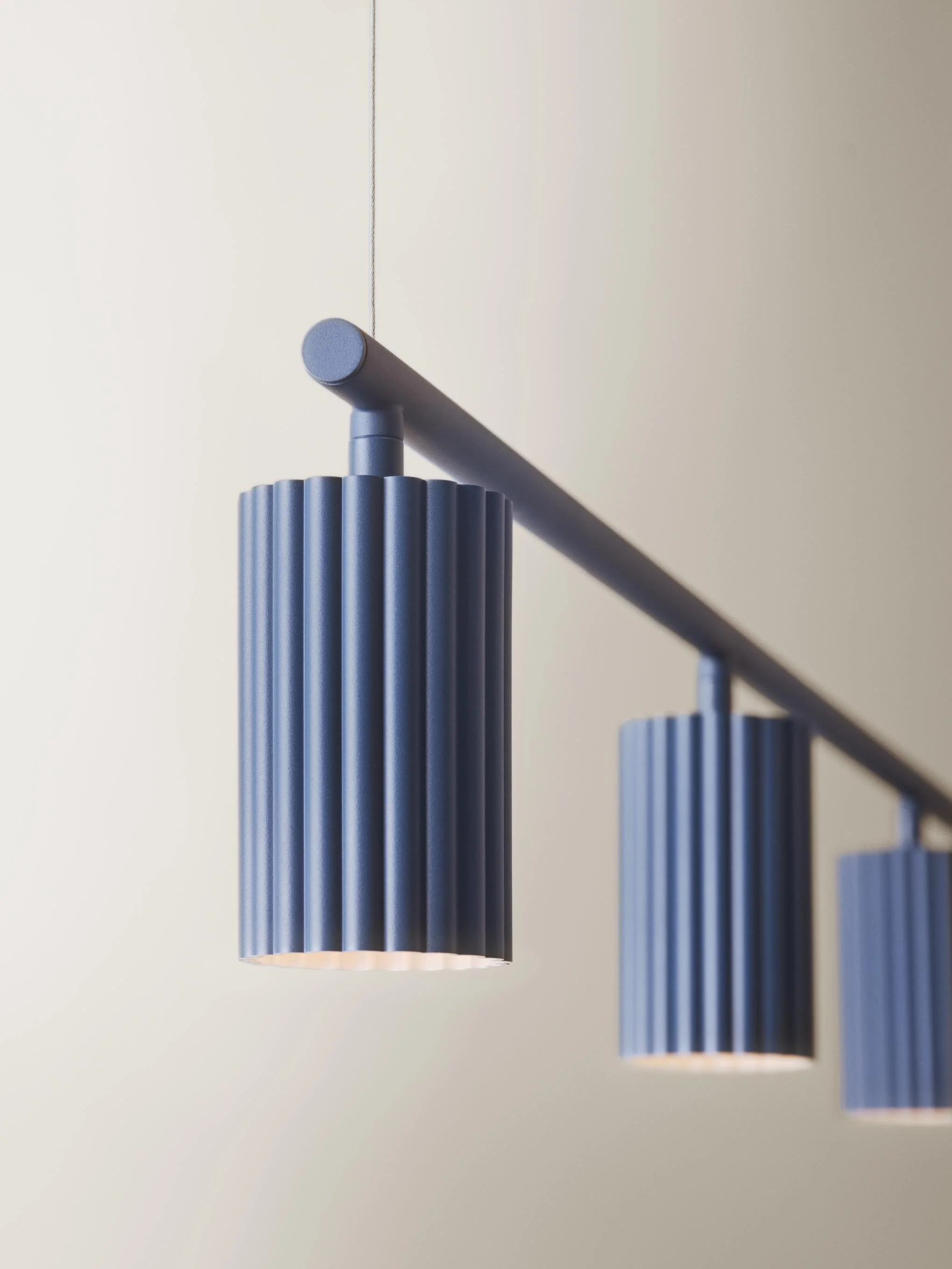 Three modern blue pendant lights with ribbed cylindrical shades hanging from a track against a plain cream wall.