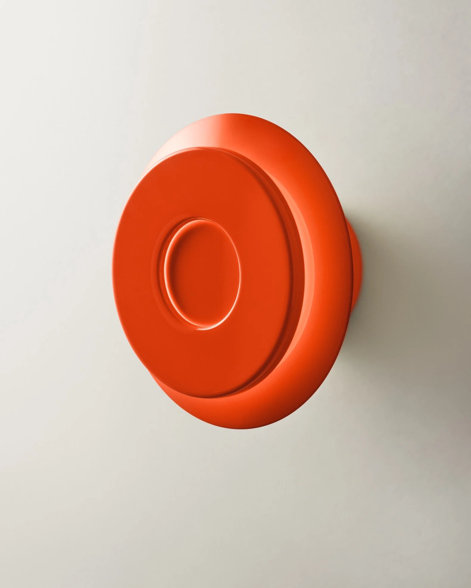 Red circular object against a light background, with a textured, shiny surface and concentric circles.