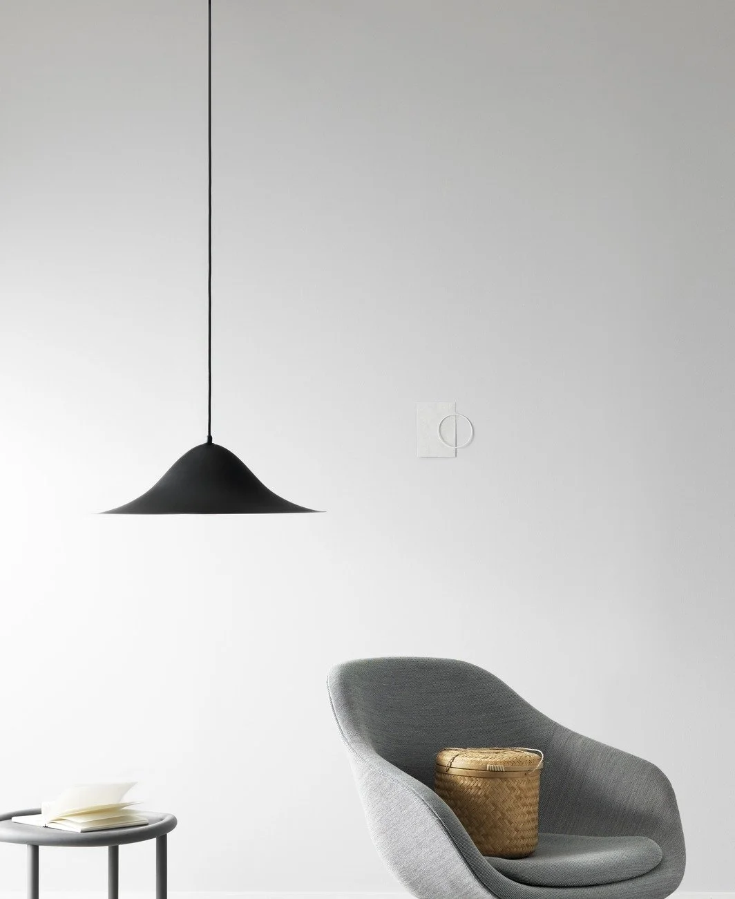 Minimalist interior with a modern gray armchair, a small side table with an open book, and a black pendant light hanging from the ceiling.