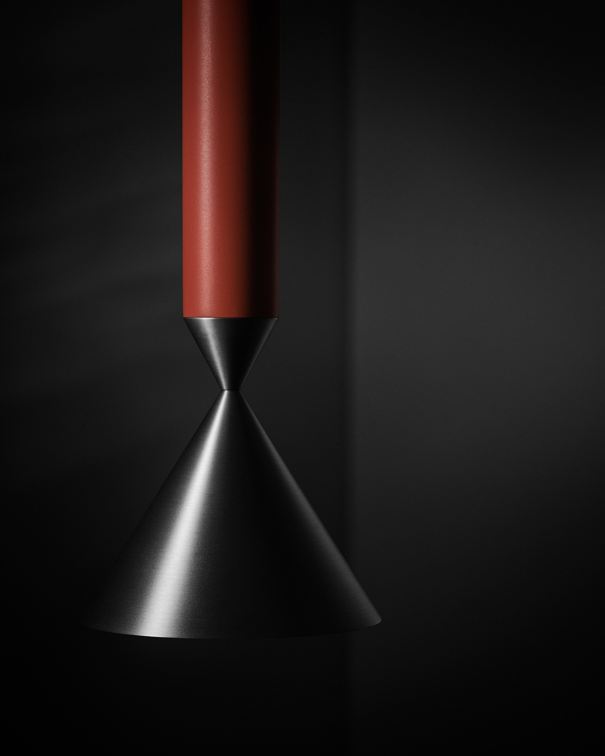 Close-up of a modern, minimalist red and black desk lamp with a conical metal shade against a dark background.
