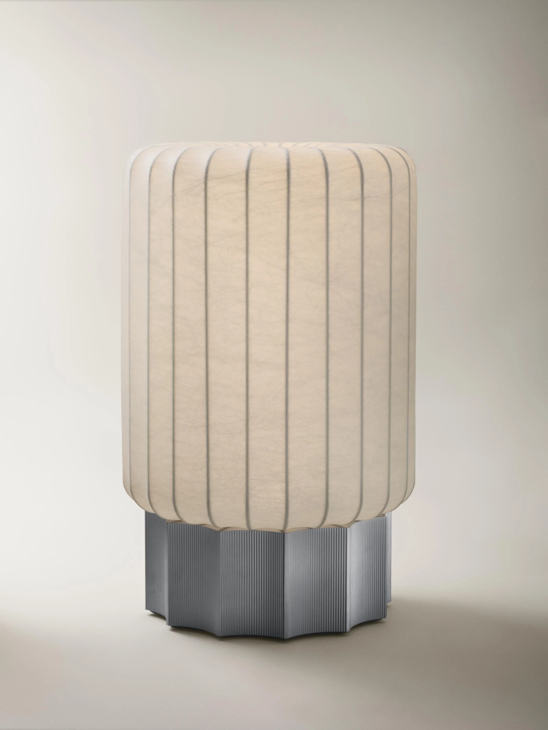 A modern lamp with a cylindrical cream-colored fabric shade with vertical black lines and a pleated, geometric metal base.