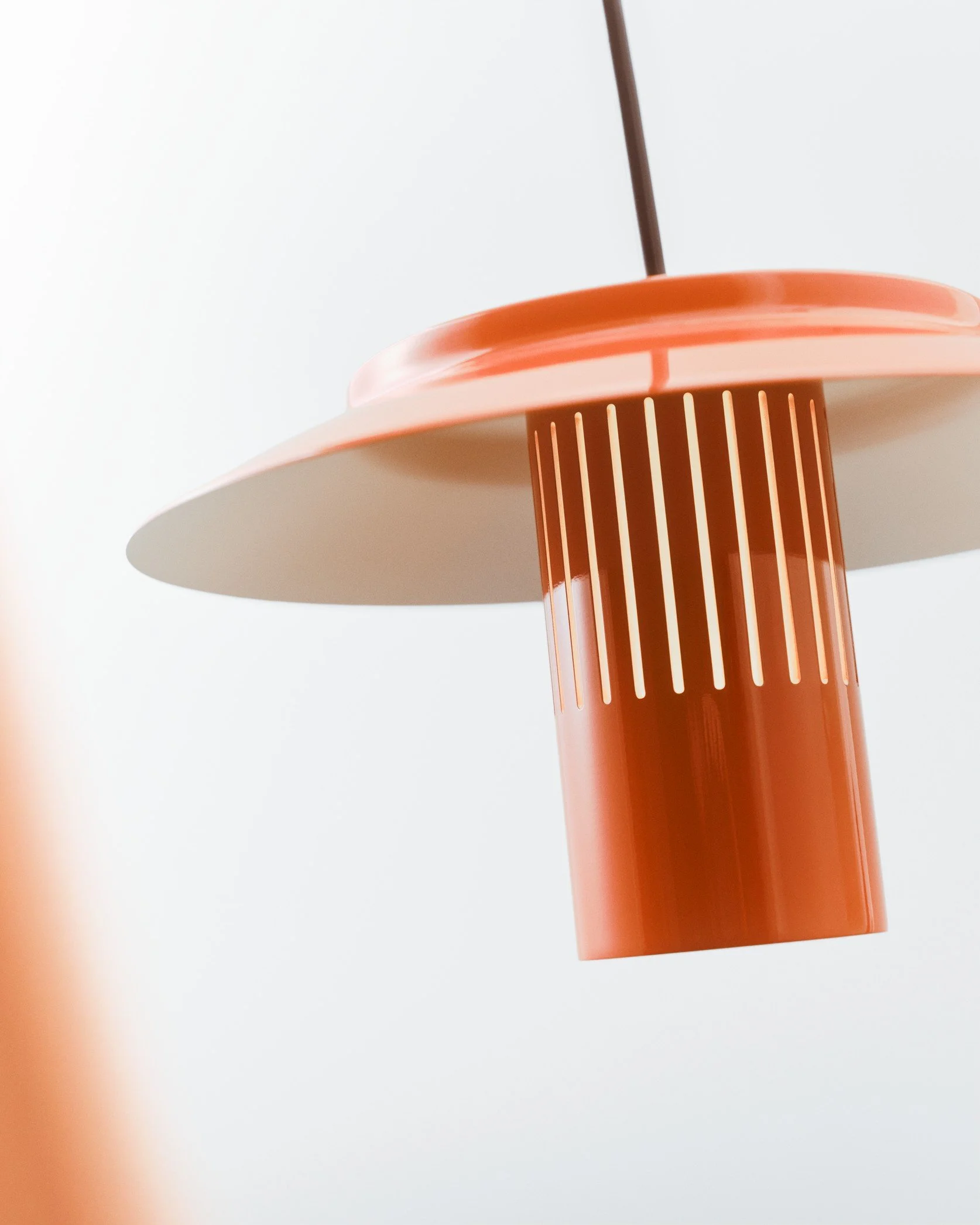 Close-up of a modern, orange-colored lamp with a round shade and slotted cylindrical base against a white background.